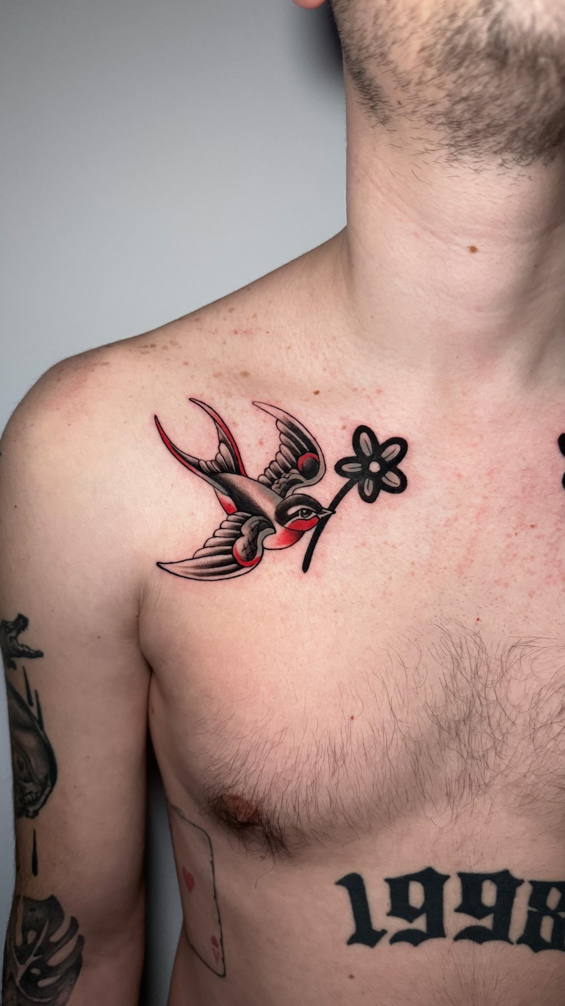 Tattoo of a swallow bird holding a flower on a person's upper chest.