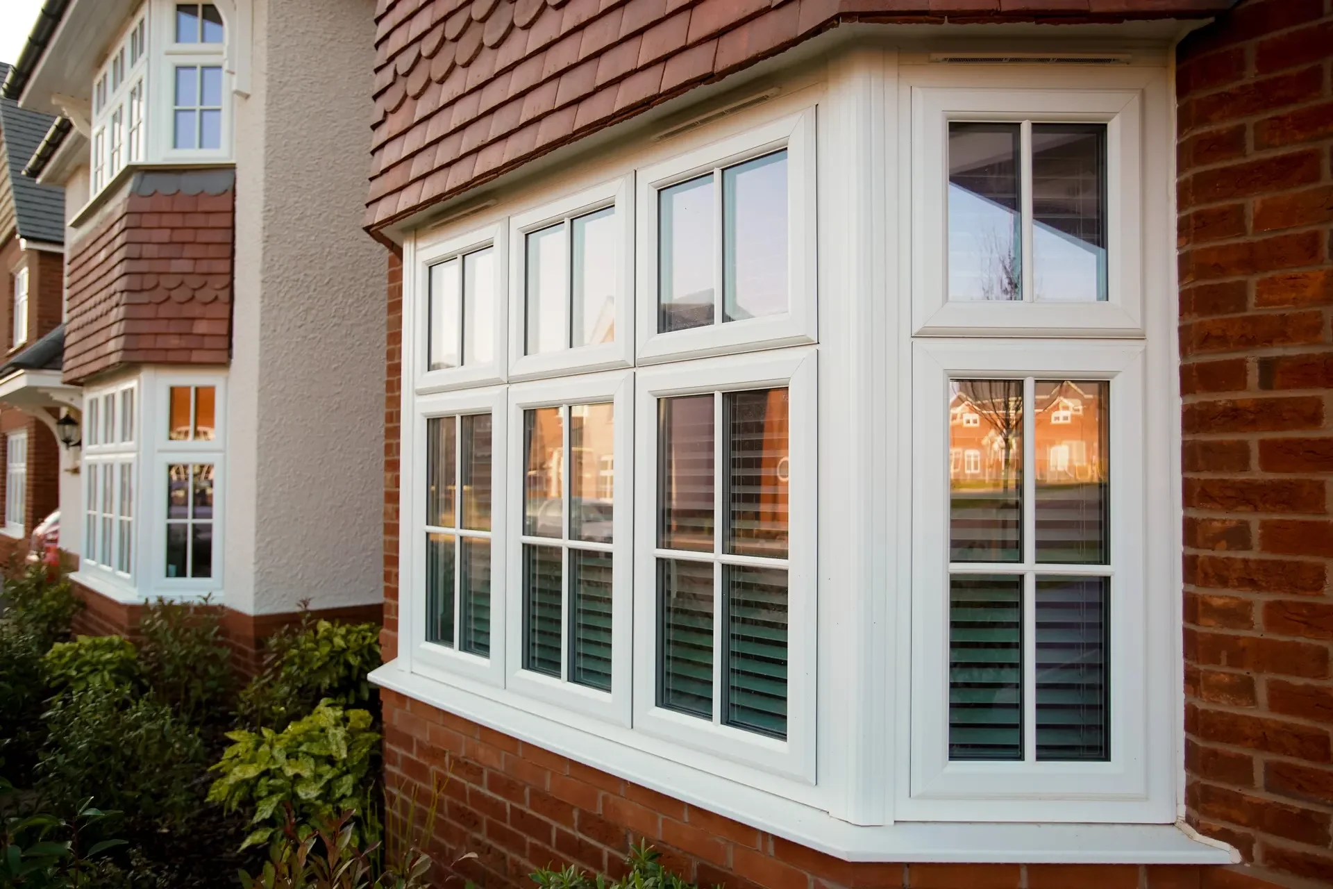 Close-up of a brick house with white framed multi-pane windows and surrounding greenery.