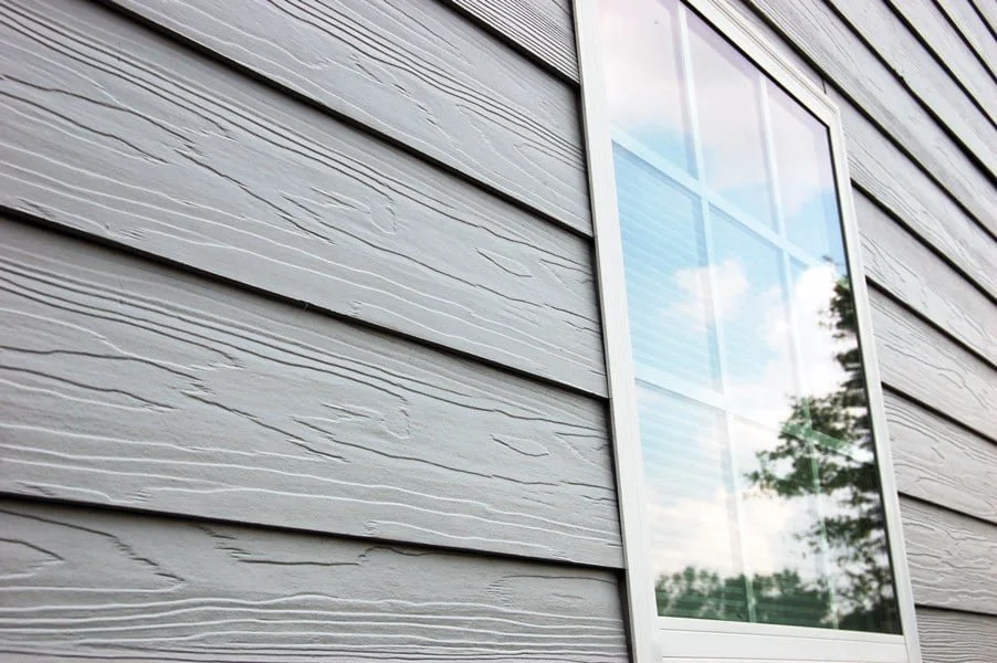 Close-up of a window on a house with wood siding, reflecting the sky and trees.
