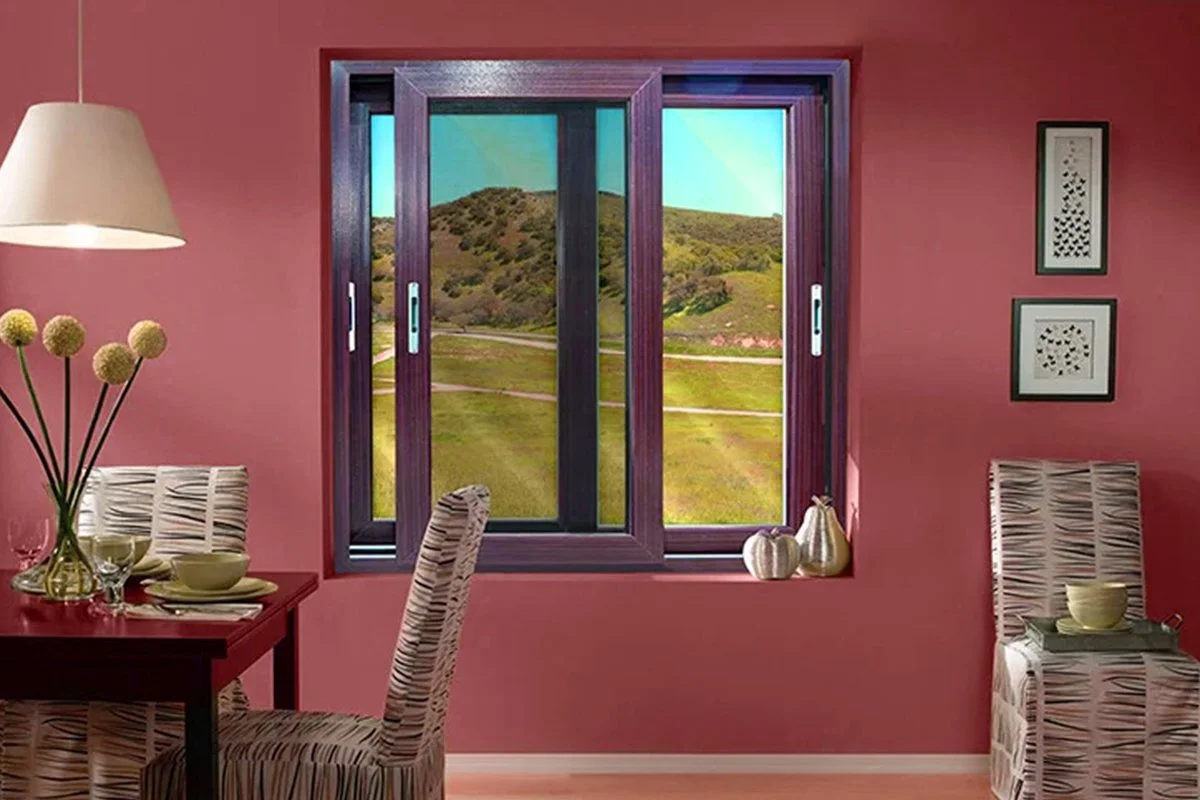 Interior of a dining room with pink walls, a window showing a scenic view of hills and green fields, a table set with plates and glasses, and a lamp hanging from the ceiling.