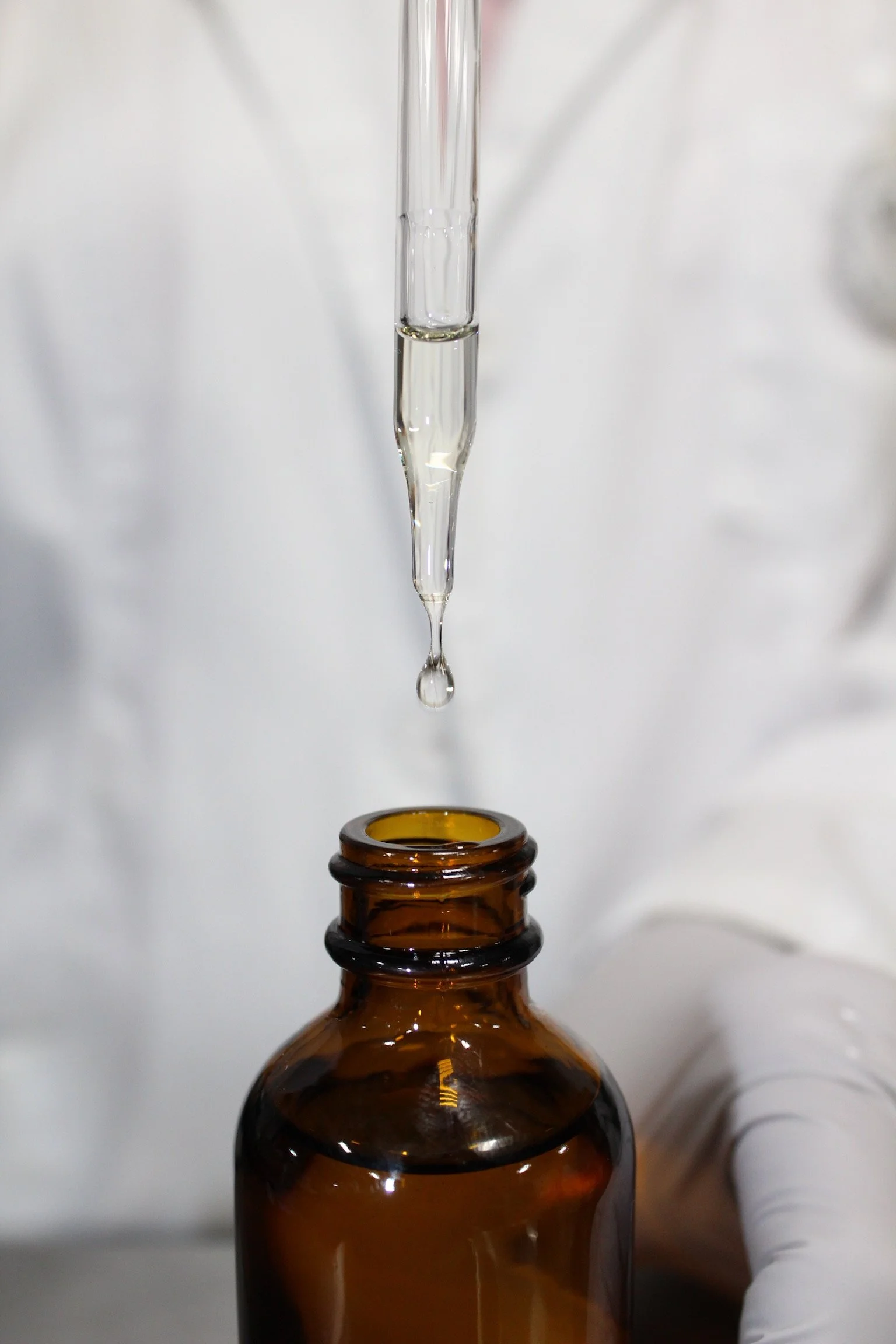 A dropper dispensing a clear liquid into a brown glass bottle.