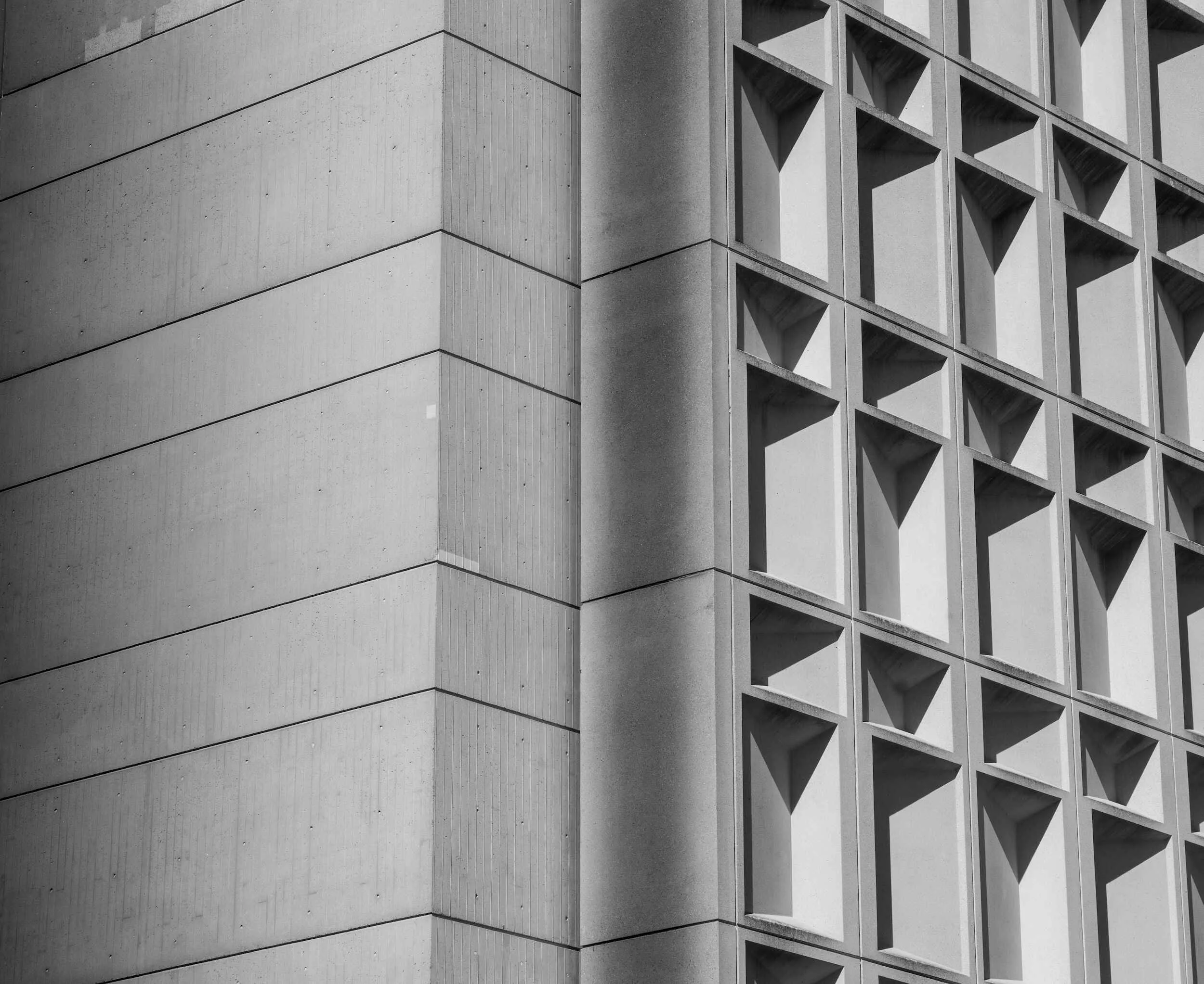 Black and white photo of a modern building with geometric architectural details, including square and rectangular concrete panels with grid-like window patterns.