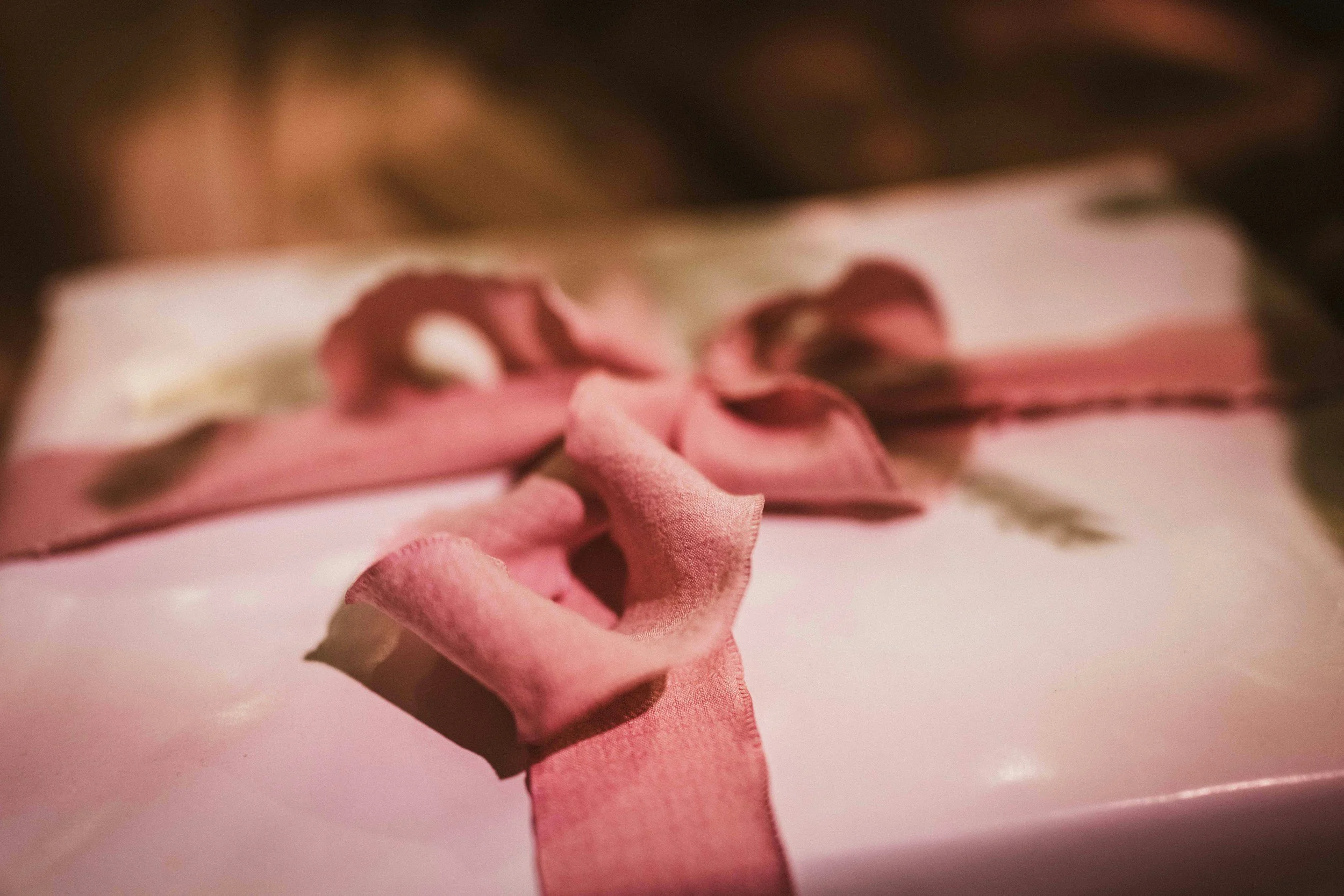 Close-up of a wrapped gift box with pink satin ribbon and bow on a surface, with a blurred background.