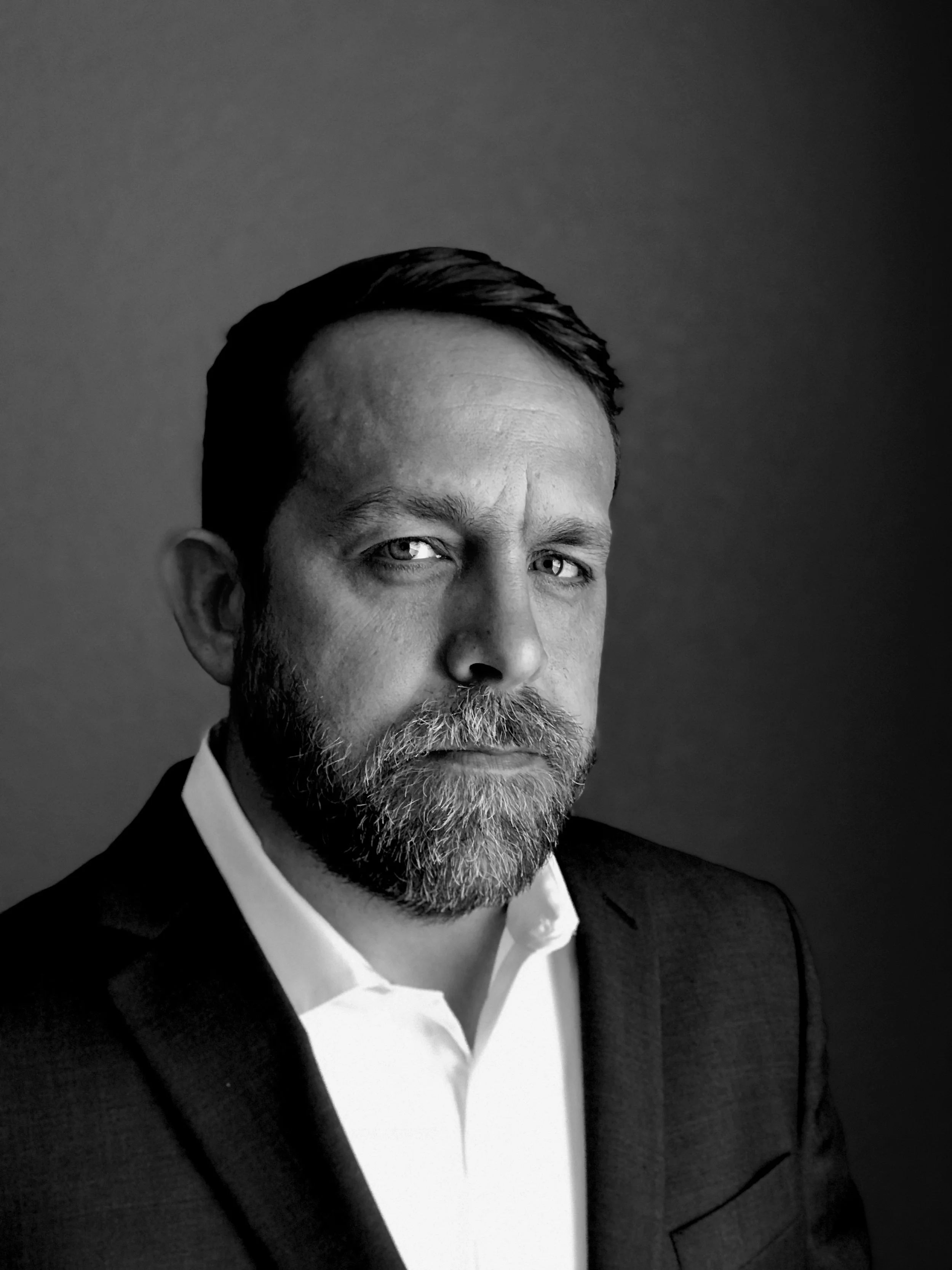 Black and white portrait of a man with a beard wearing a suit and white shirt, looking serious.