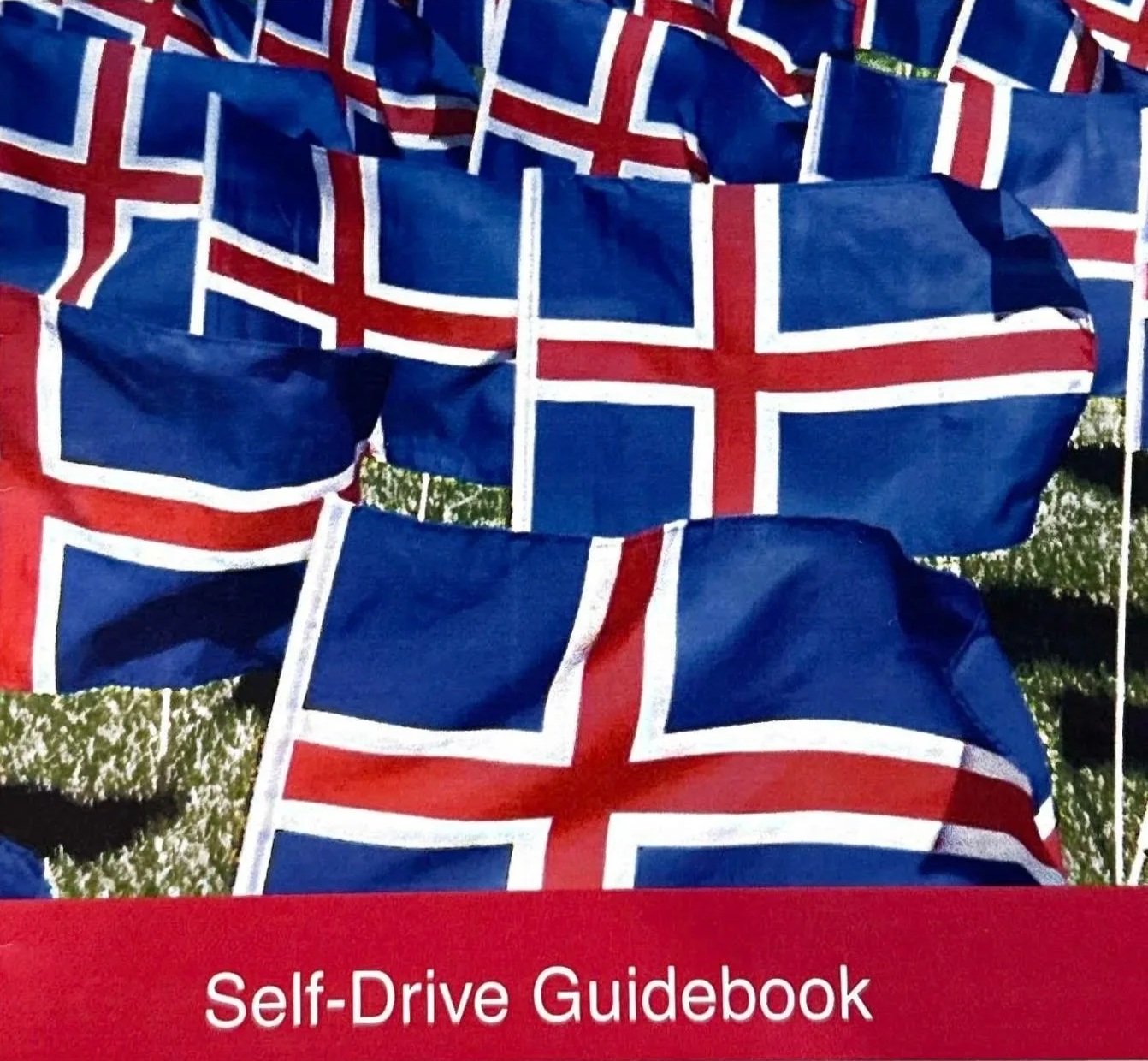 A close-up view of multiple Icelandic flags on display, with a red banner at the bottom reading "Self-Drive Guidebook." It was created by Sunna and shows all the locations of Icelandic churches, cemeteries, memorial sites, and locations.