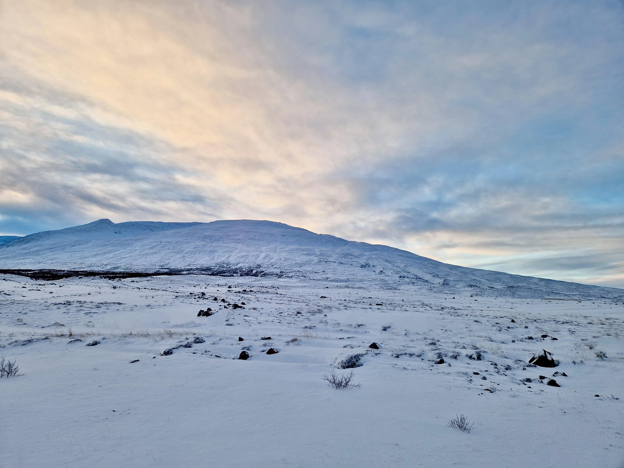 Snow-covered mountain landscape with a partly cloudy sky during sunset or sunrise.
