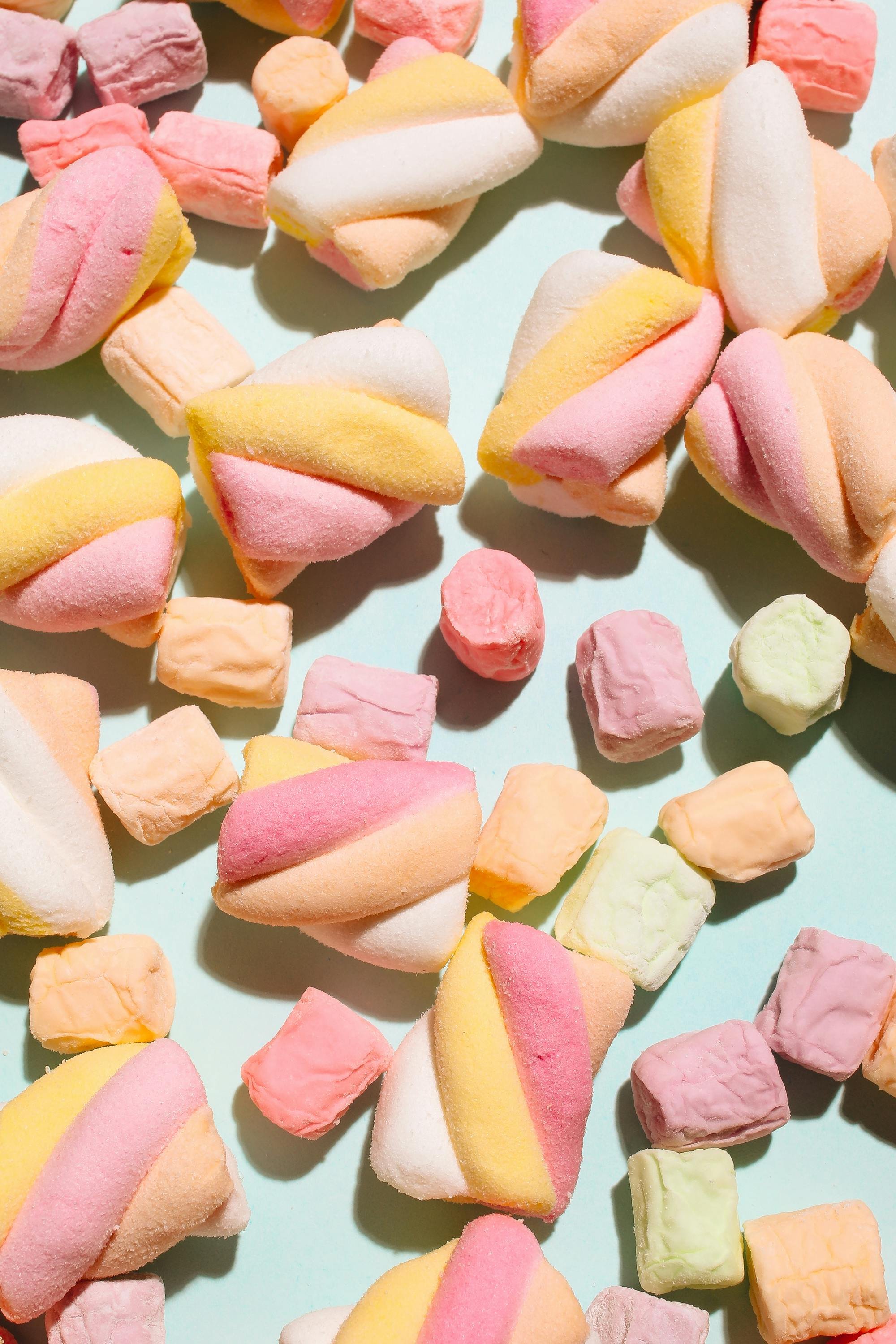 Colorful marshmallow candies in pastel shades, including pink, yellow, white, and peach, scattered on a light blue surface.