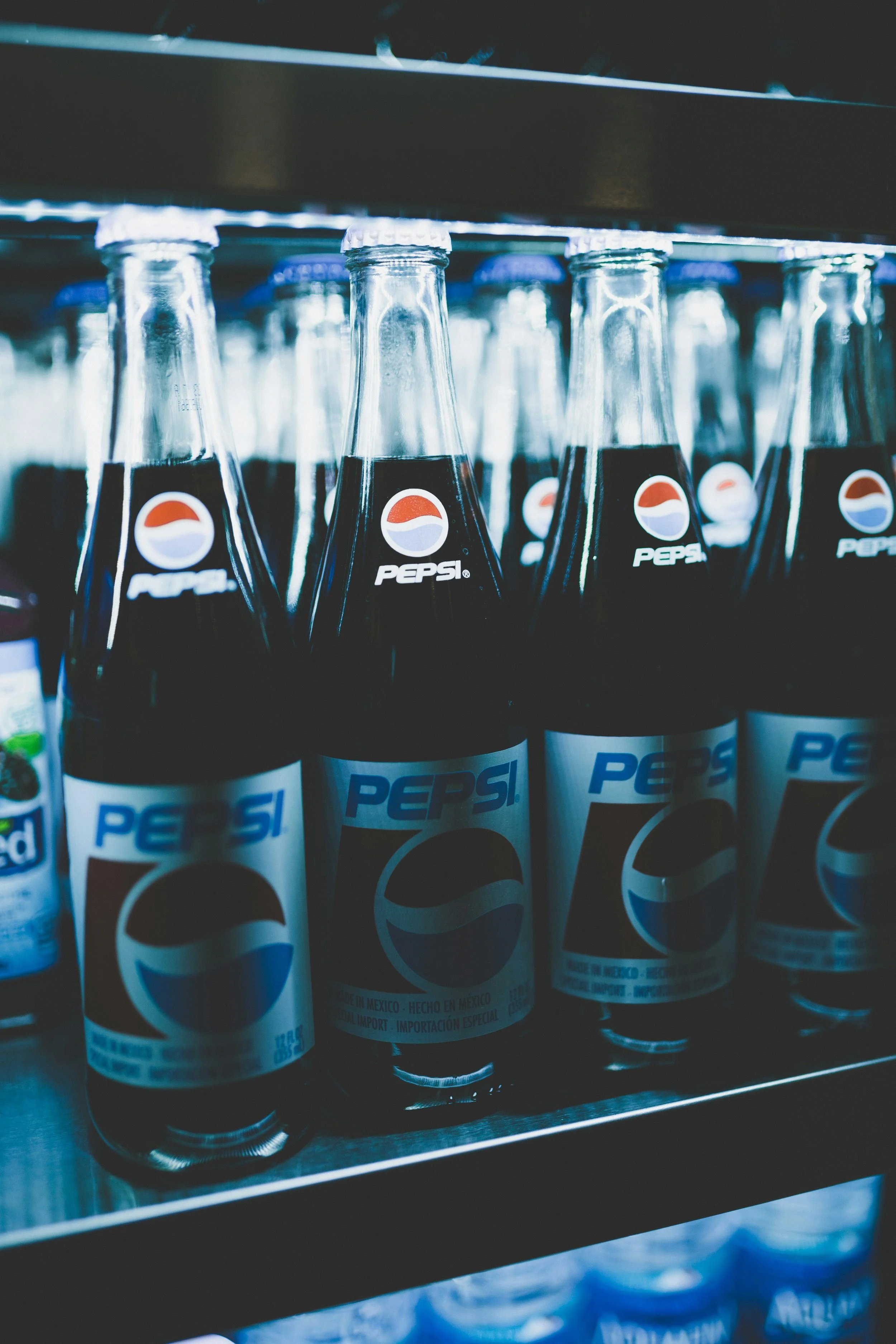 Several glass bottles of Pepsi soda on a metal shelf in a store.