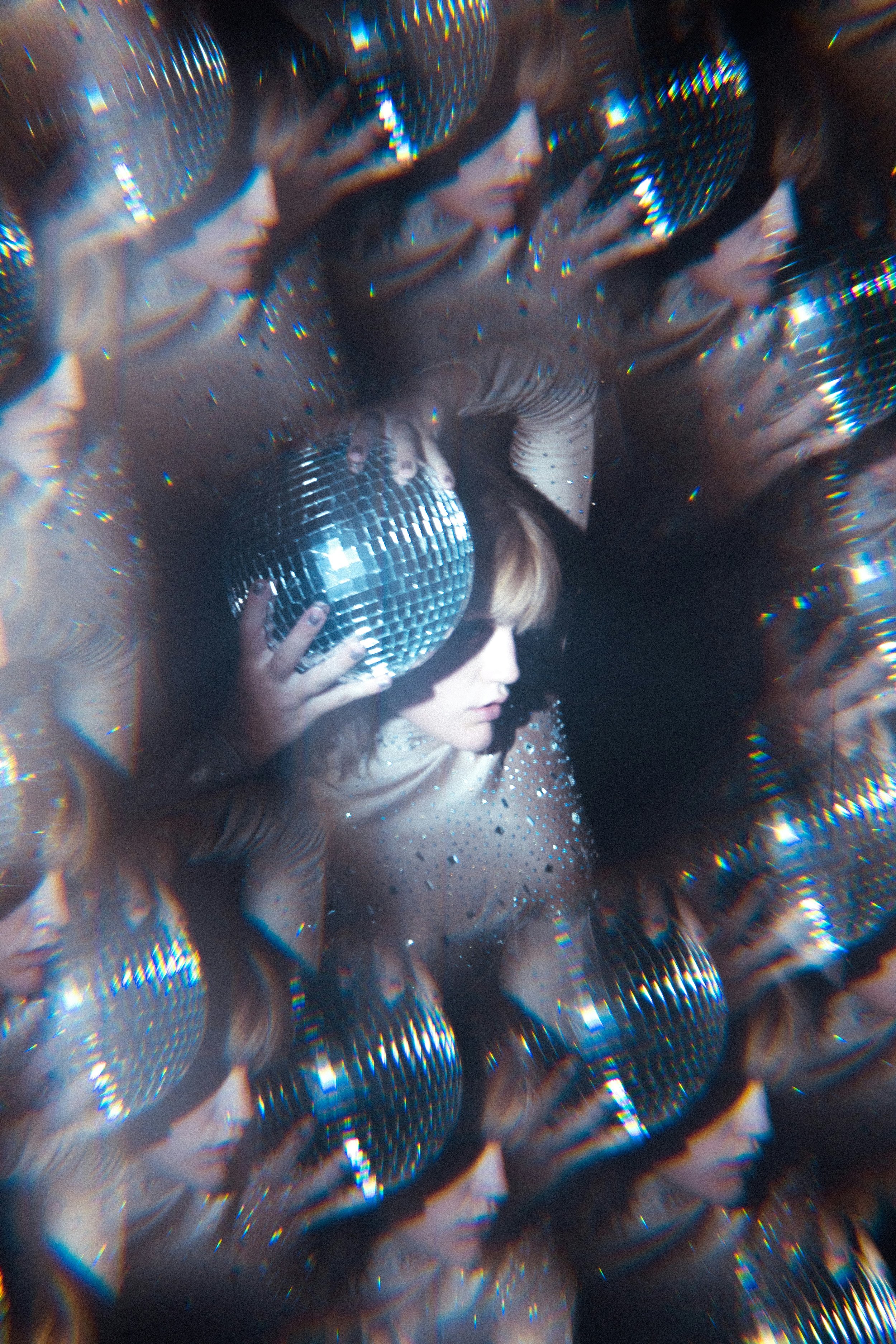 A person with brown hair dancing in front of shiny disco balls, illuminated with colorful lights, creating a vibrant and energetic atmosphere.