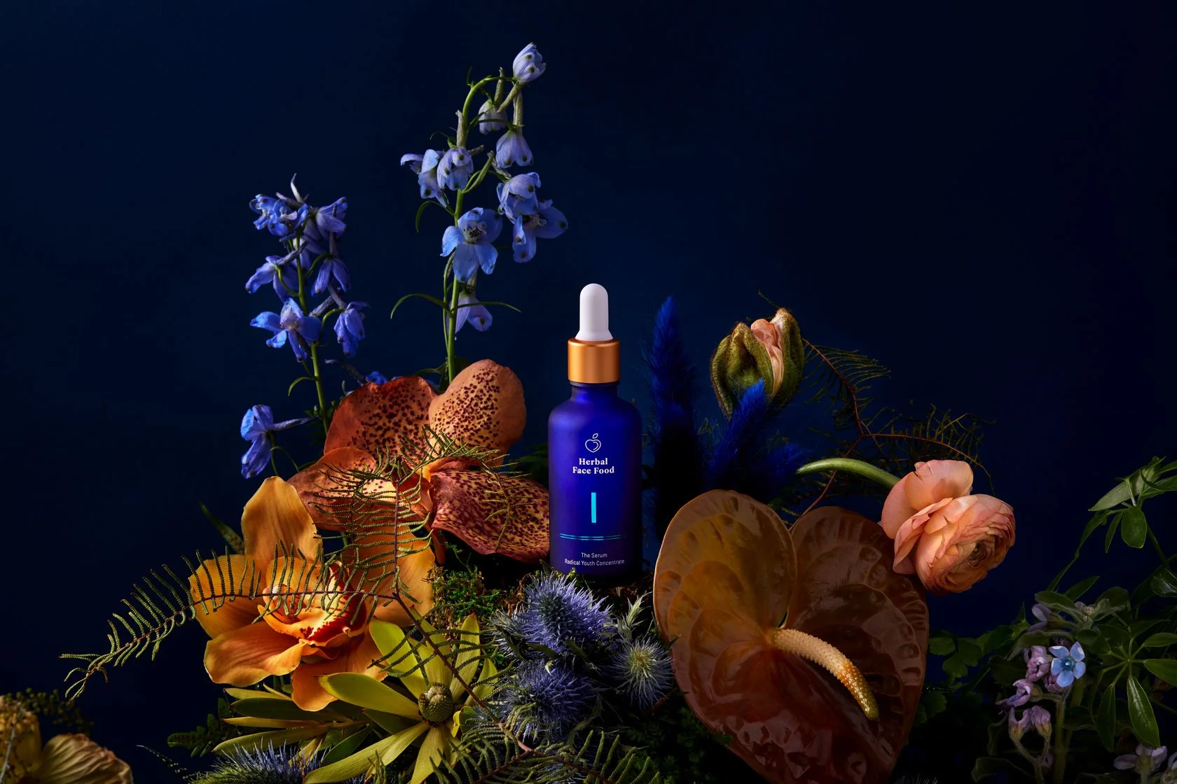 A blue botanical bottle with a dropper cap surrounded by various colorful flowers and plants on a dark background.