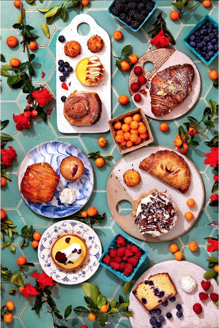 Assorted baked goods and fresh berries arranged on decorative plates and a tiled surface, surrounded by orange and red berries and green leaves.