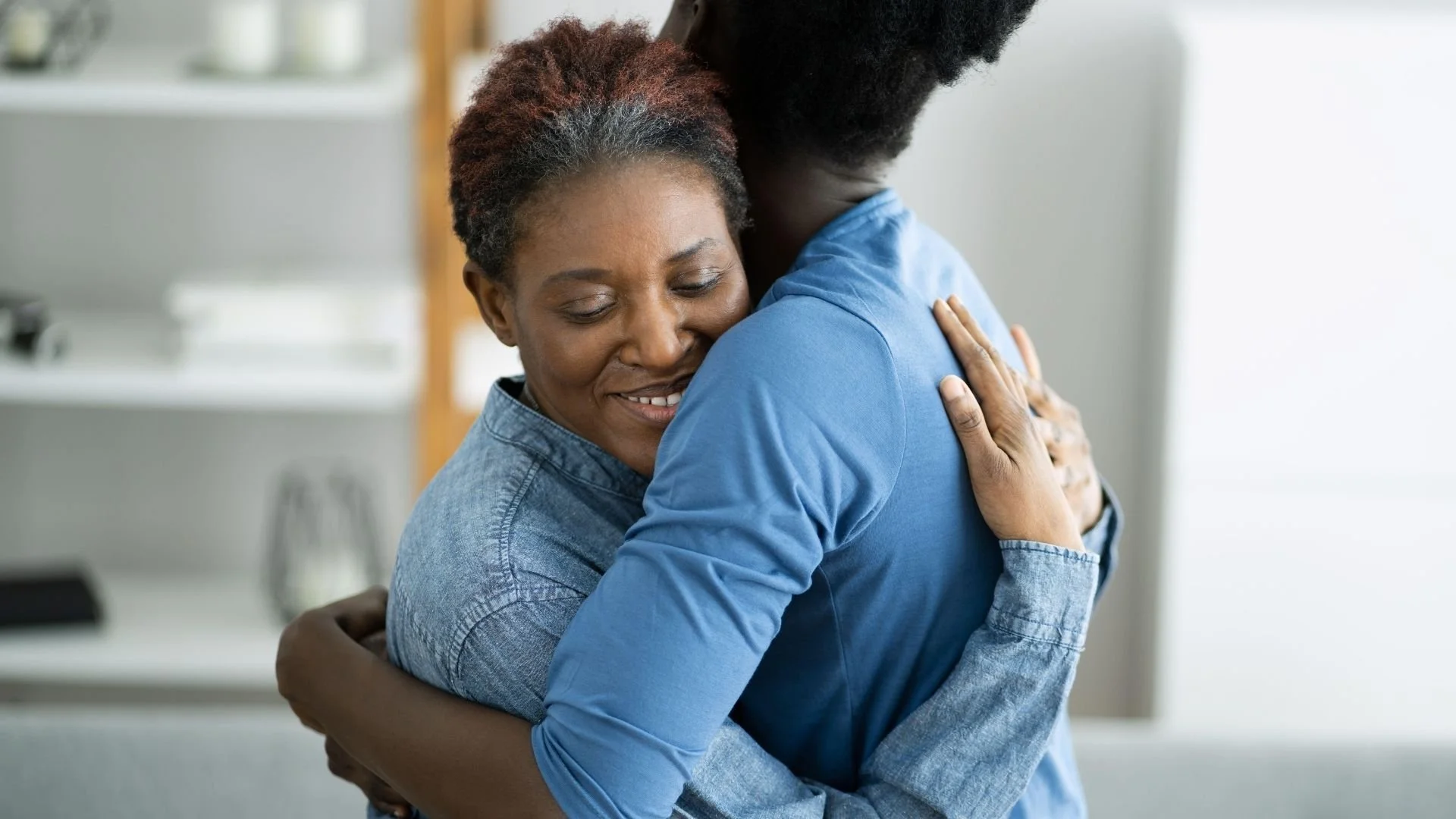 Two women hugging in a warm embrace, smiling peacefully.