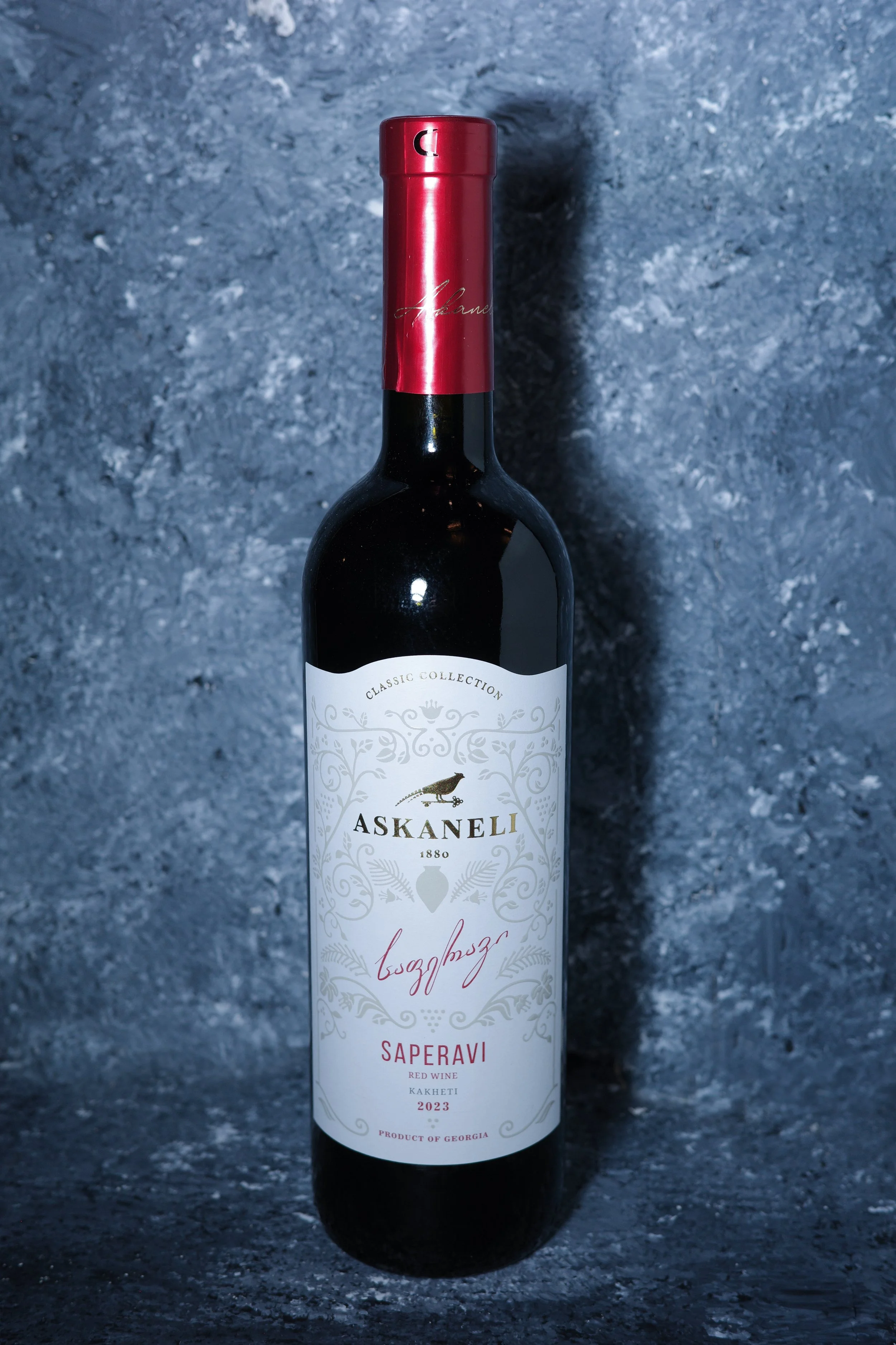 A bottle of Askaneli Saperavi red wine from Georgia, vintage 2023, with a red foil top and a white label.