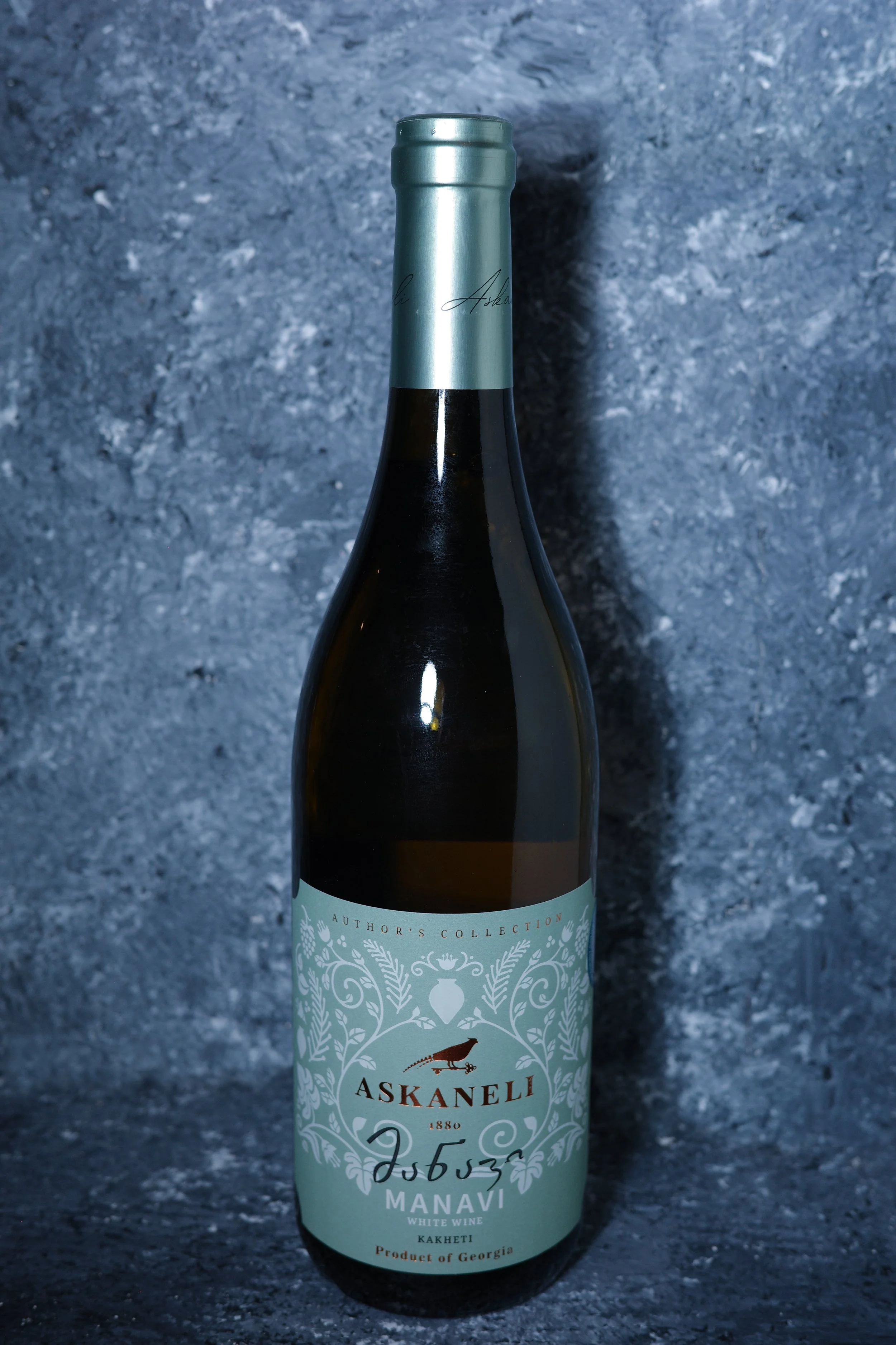 A bottle of white wine with a light blue label and metallic cap, featuring a bird and decorative design, against a textured gray background.