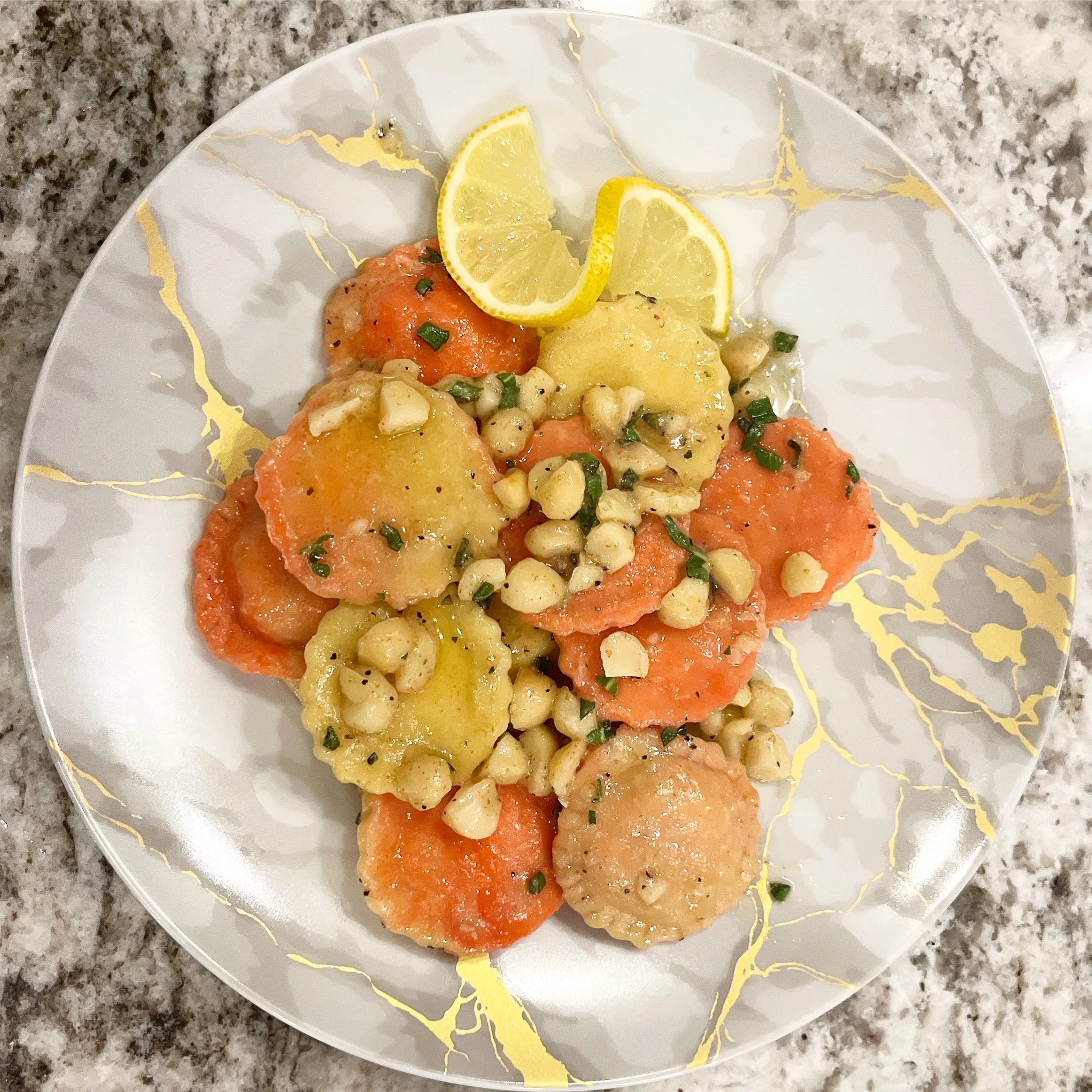 Plate of colorful boiled or steamed carrots and potatoes garnished with chopped herbs, chopped nuts, and lemon wedges, on a decorative white plate with gold accents, on a speckled gray countertop.