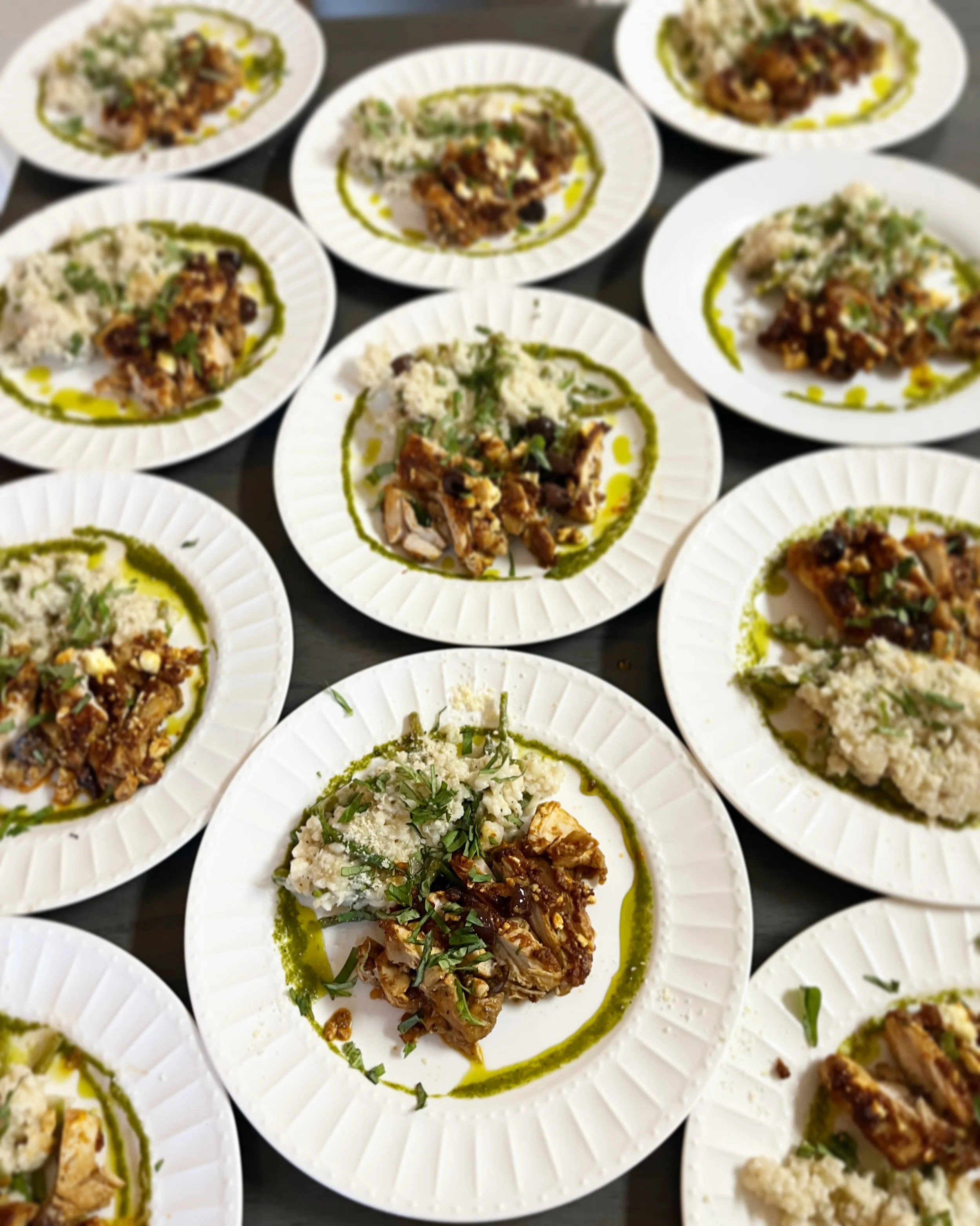 Multiple white plates with servings of pulled pork, mashed potatoes or rice, garnished with herbs, and drizzled with green sauce.