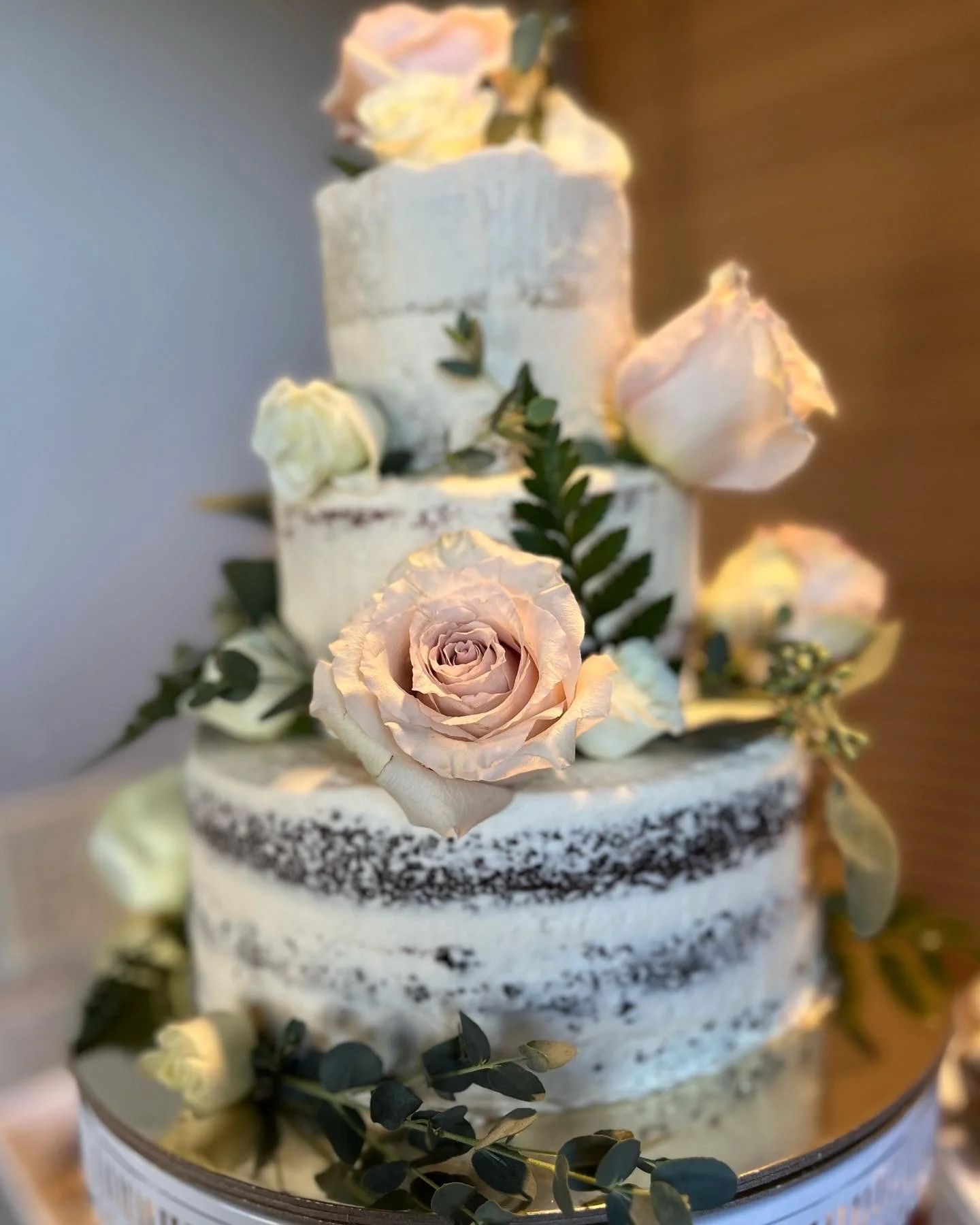 A multi-tiered wedding cake decorated with pale pink roses and eucalyptus leaves.