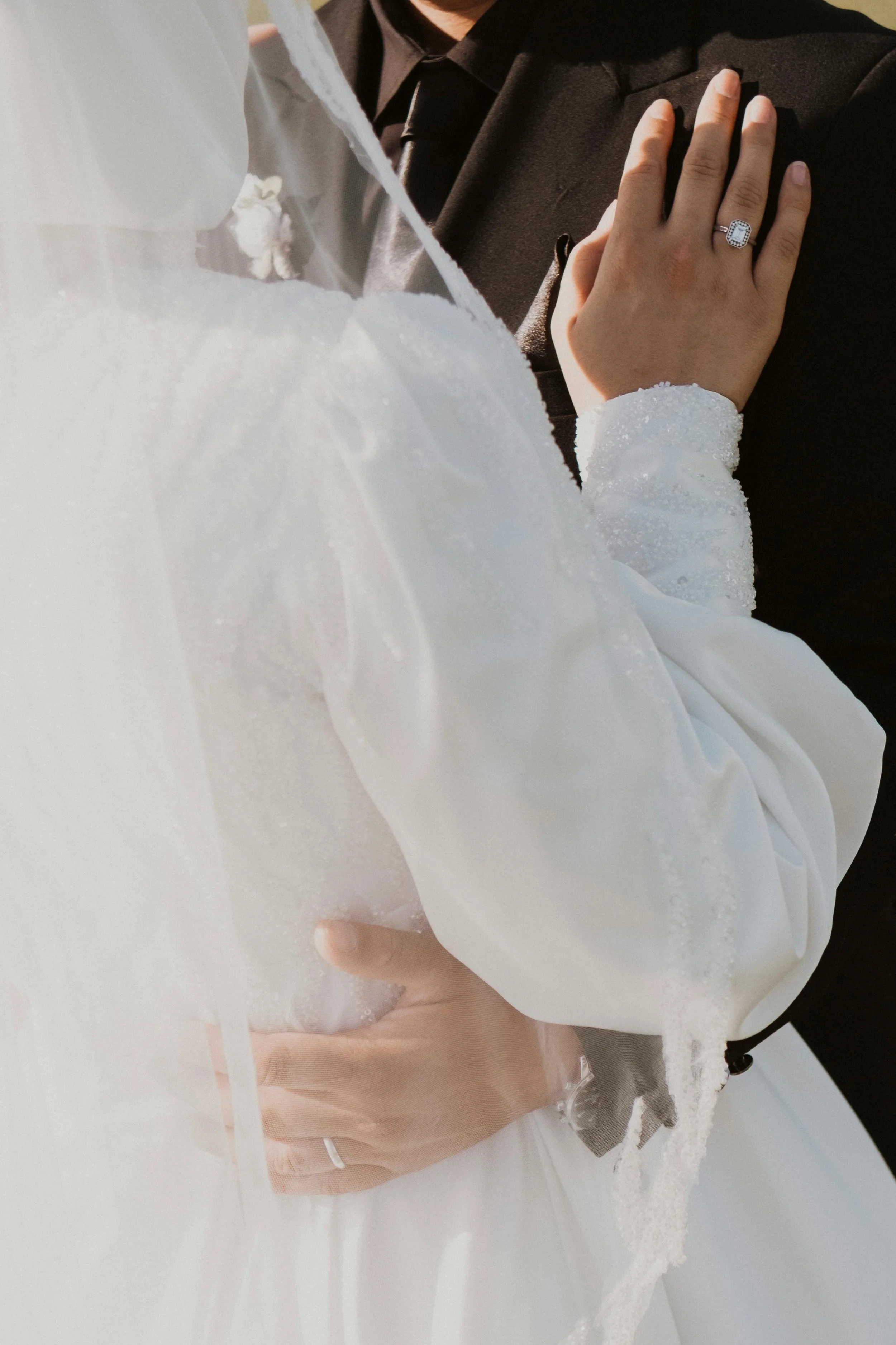 Close-up of a bride and groom holding hands, with the bride's hand showing an engagement ring, during their wedding ceremony.