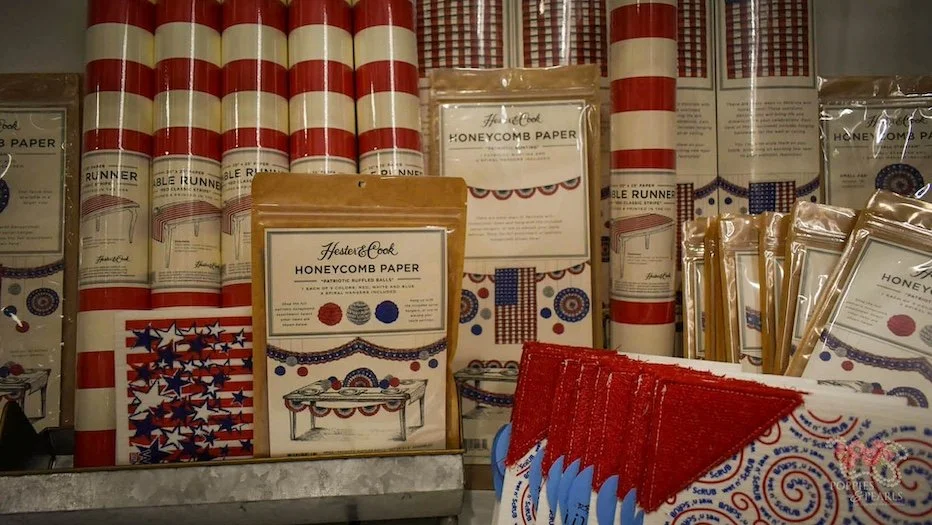 Patriotic-themed party supplies with red, white, and blue designs, including table runners, napkins, and honeycomb paper decor.