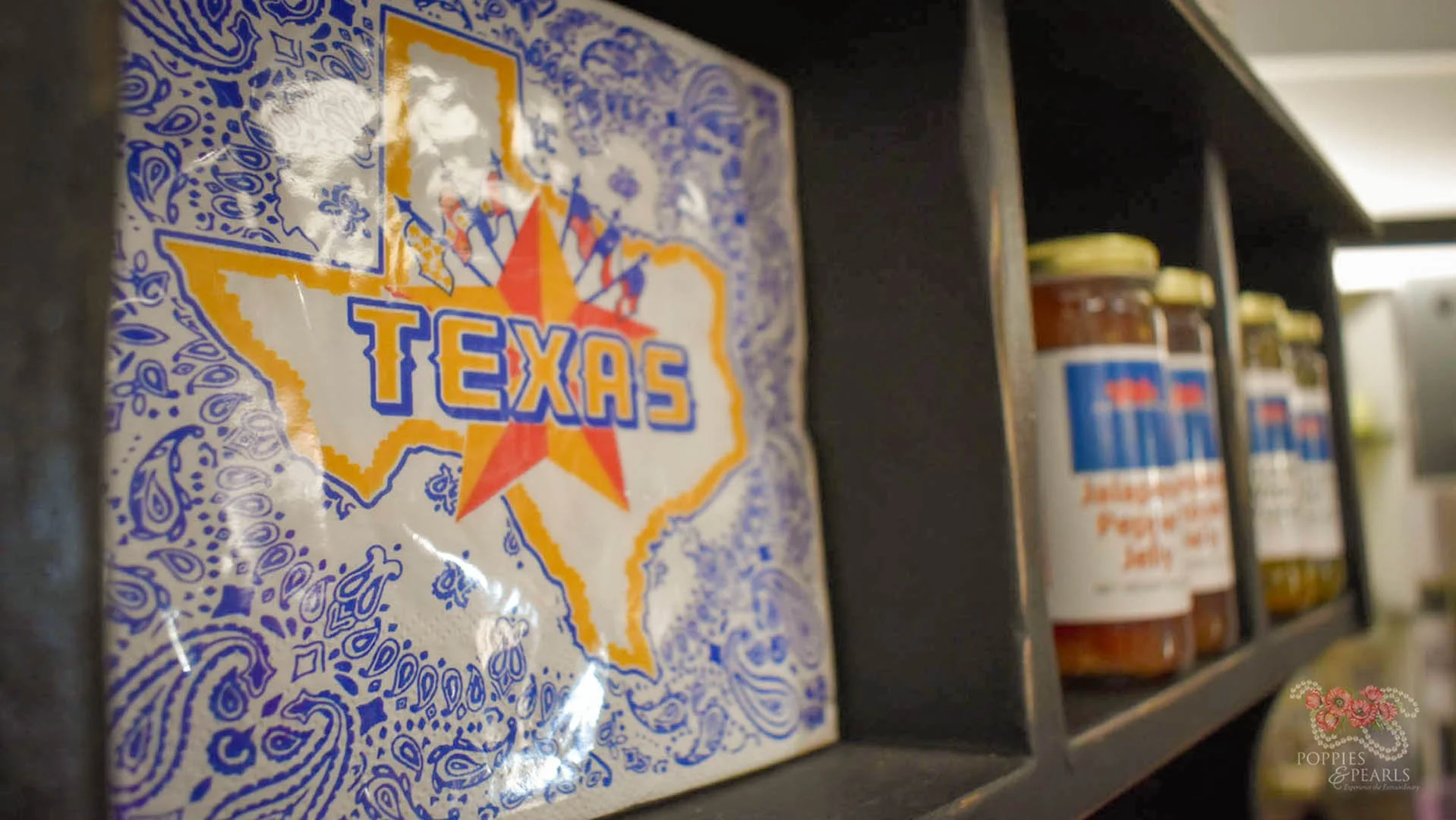 Close-up of a Texas-themed souvenir magnet with a star and the outline of Texas, placed on a dark shelf with jars of condiments in the background.