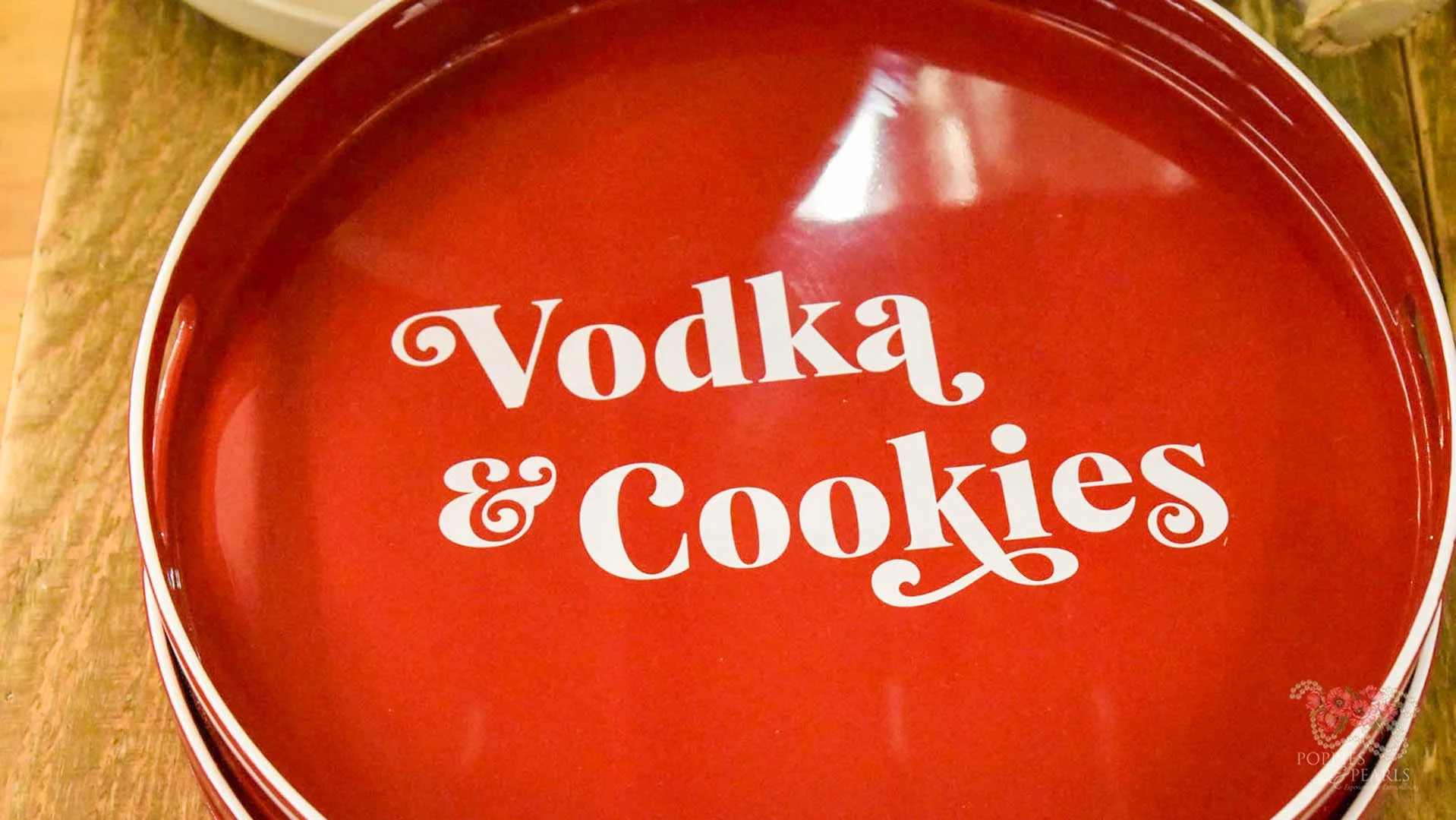 A red round tray with white text that reads 'vodka & Cookies' inside, resting on a wooden surface.