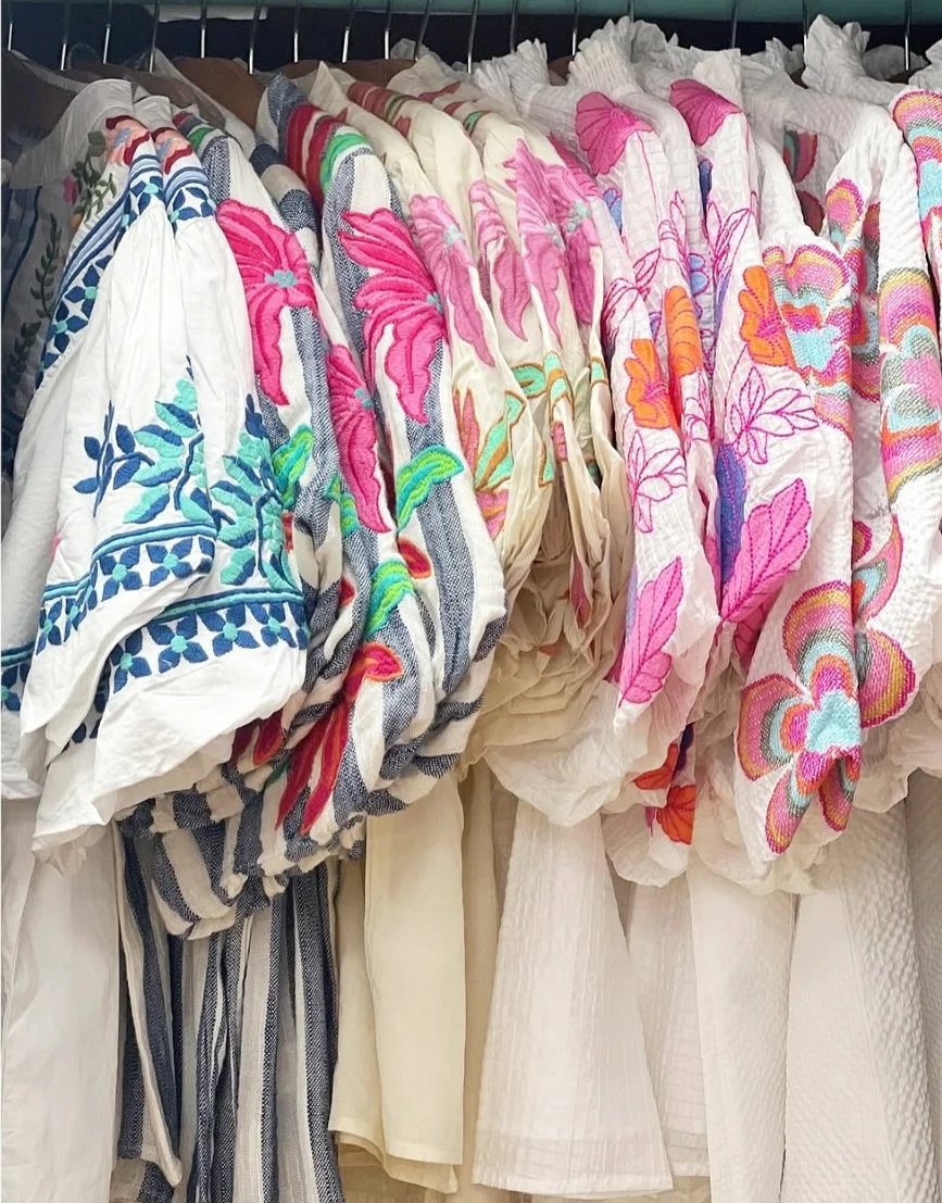 Clothes with colorful embroidered floral designs hanging on a rack.
