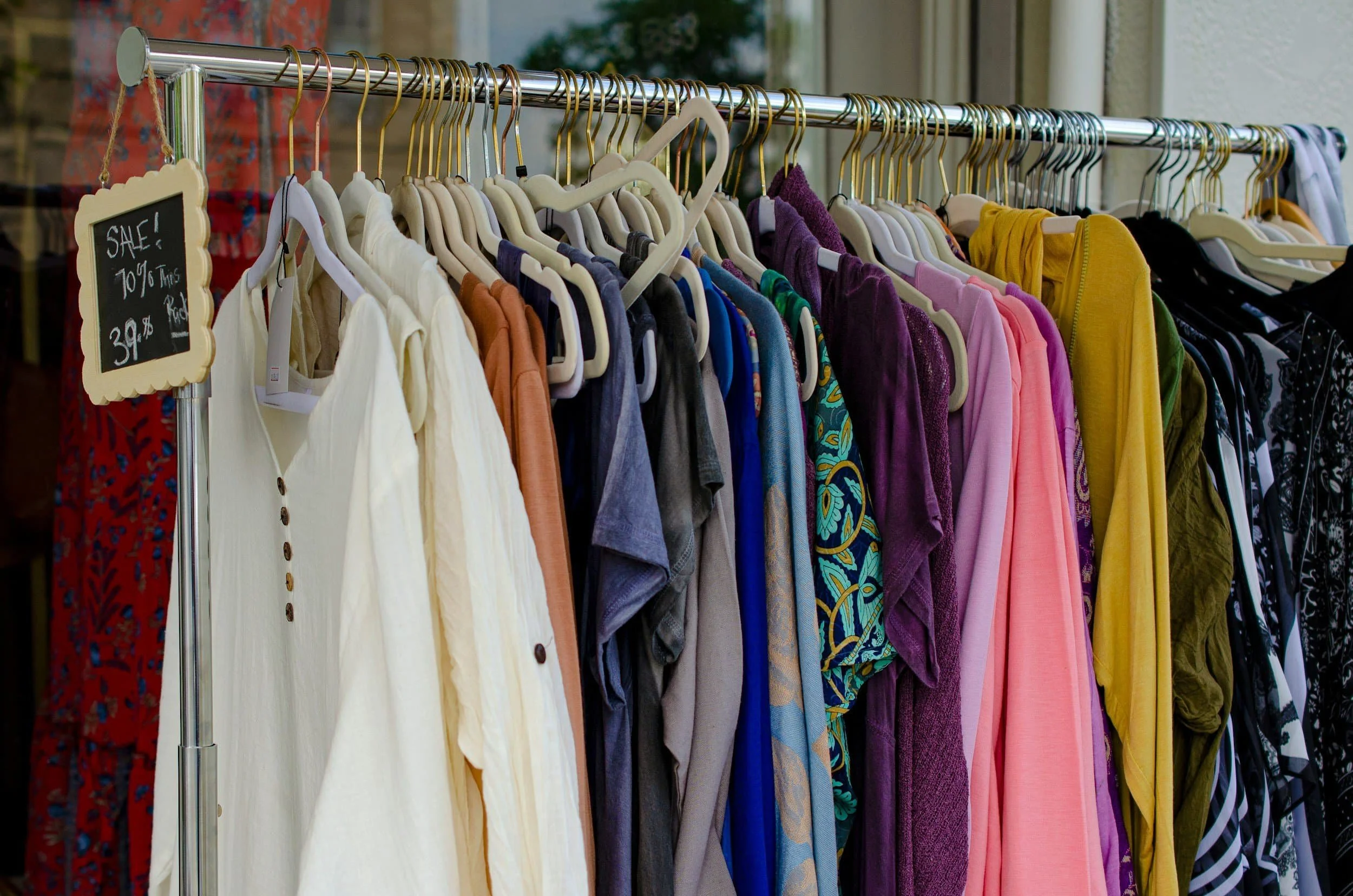 Clothing rack with various colorful garments including shirts, dresses, and skirts at a thrift store or clothing sale.