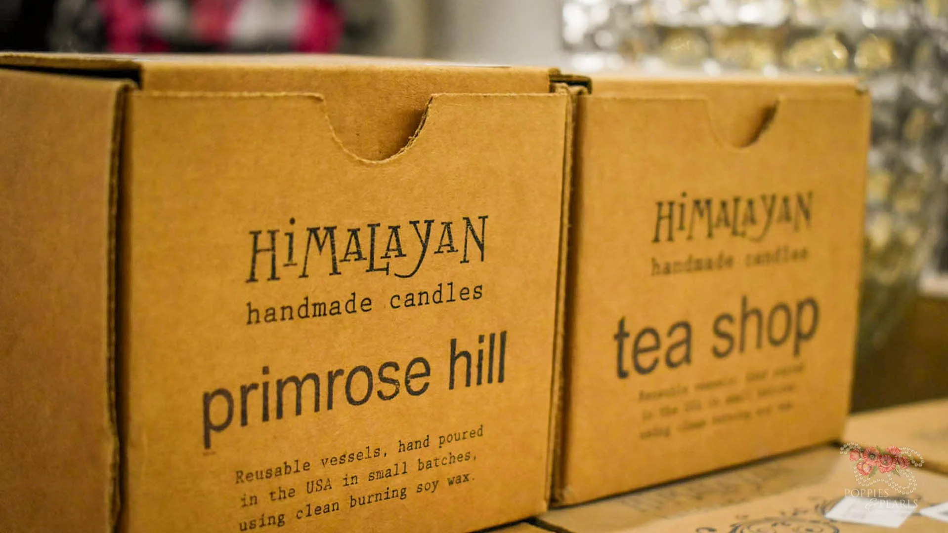 Brown cardboard boxes with black text displaying 'HIMALAYAN handmade candles' and product names 'primrose hill' and 'tea shop' on a store shelf.