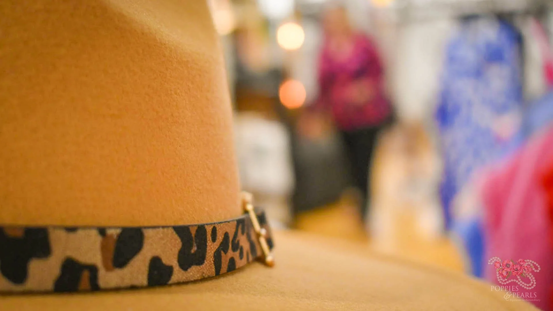 Close-up of a mustard-colored hat with a leopard-print band and small gold embellishment, with blurred people in the background.