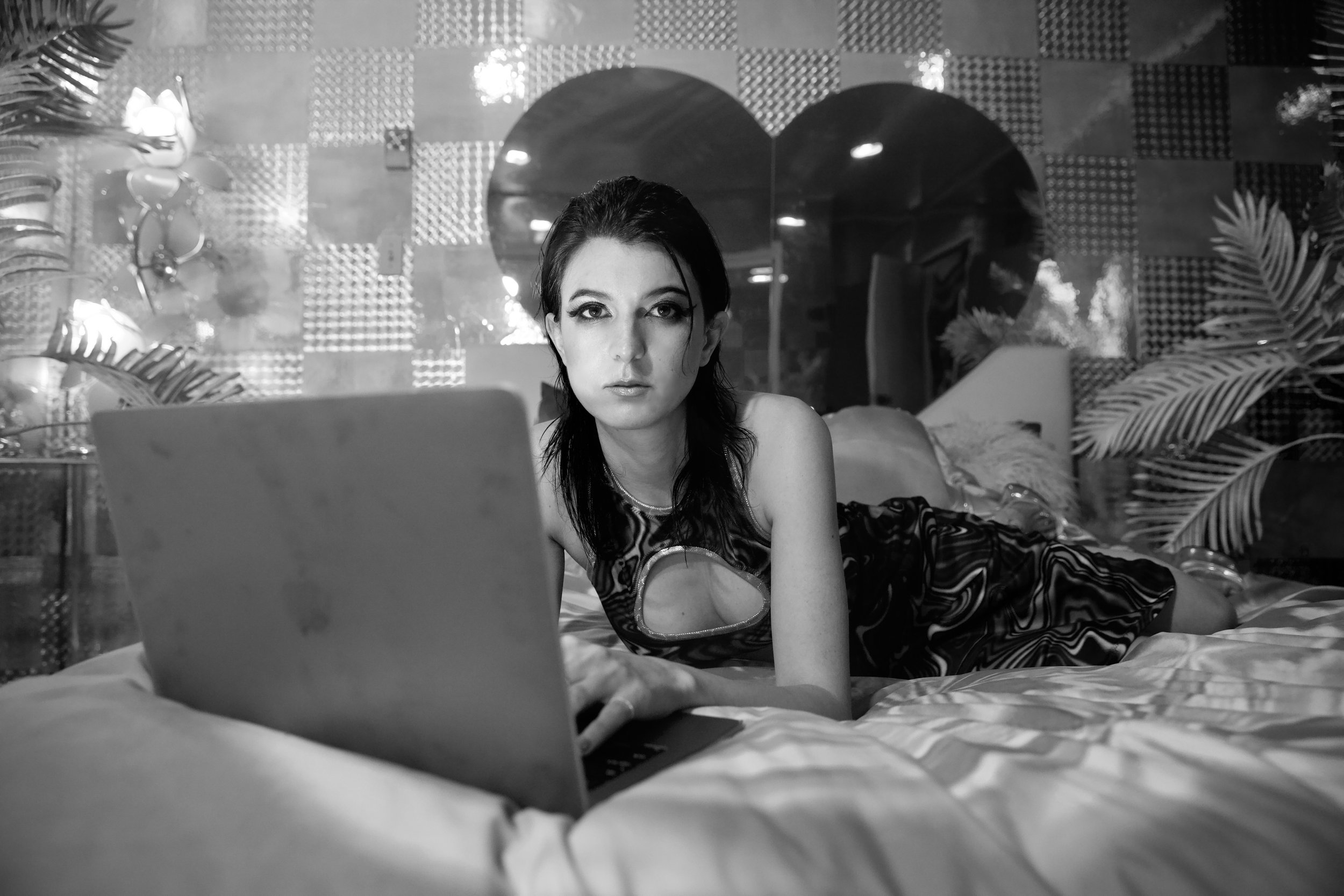 Screenwriter, Author, and Filmmaker Isa Mazzei lays in a bed and types into a laptop