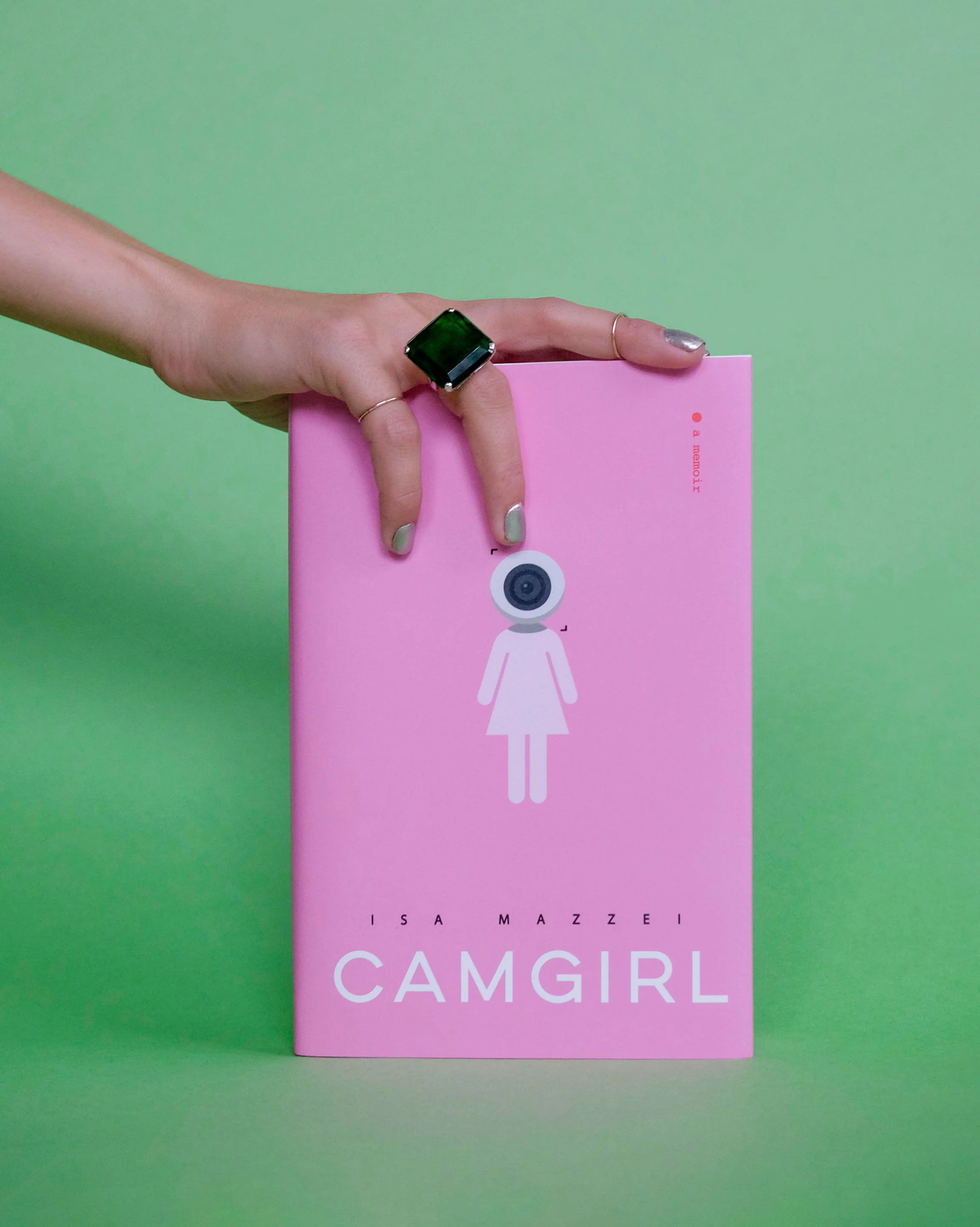 Writer Isa Mazzei holds a copy of her memoir Camgirl, by Isa Mazzei. The cover is pink and features a female figure with a webcam for a head.