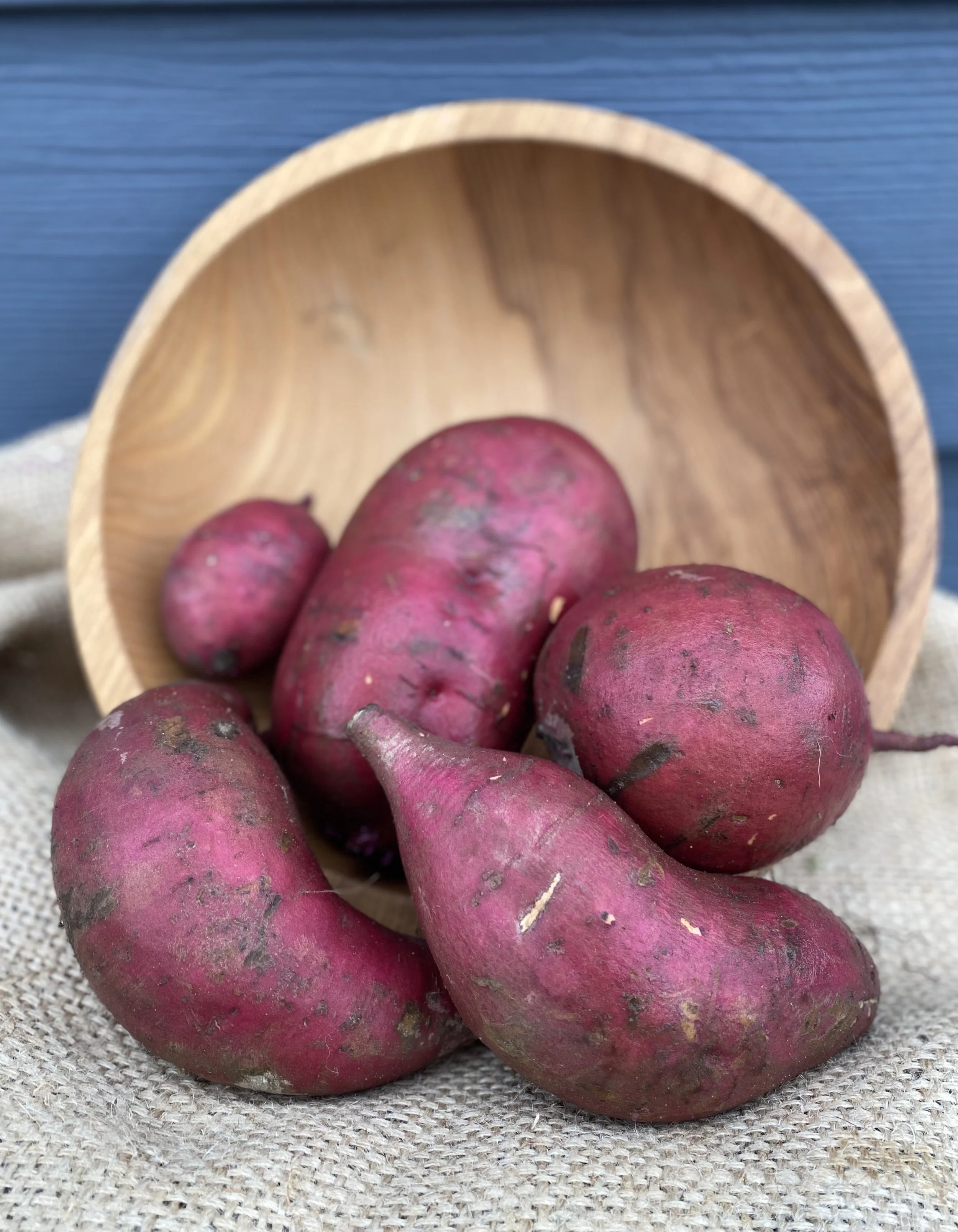 Fresh red potatoes placed on burlap fabric with a wooden bowl in the background.