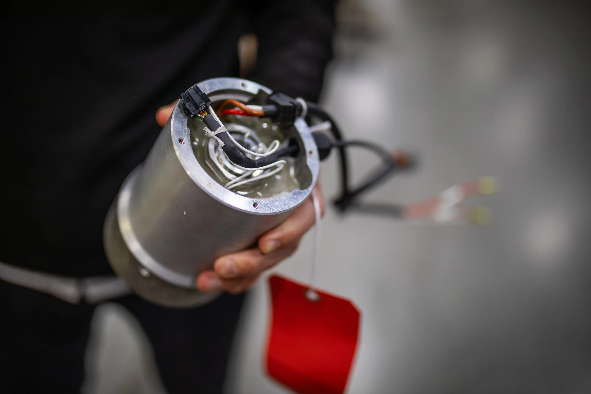 Person holding a cylindrical metal device with internal wires and electronic components.