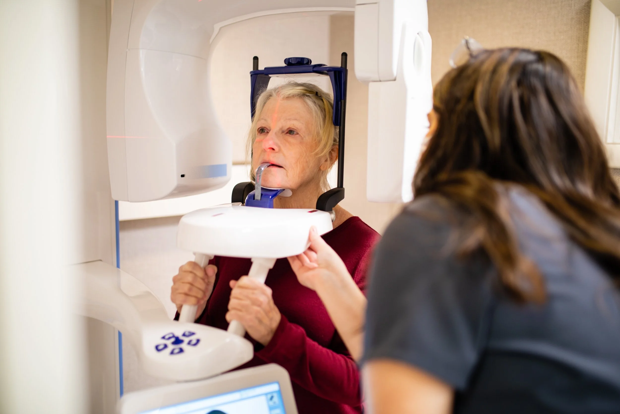 An elderly woman undergoing a medical imaging scan while a healthcare professional assists her.