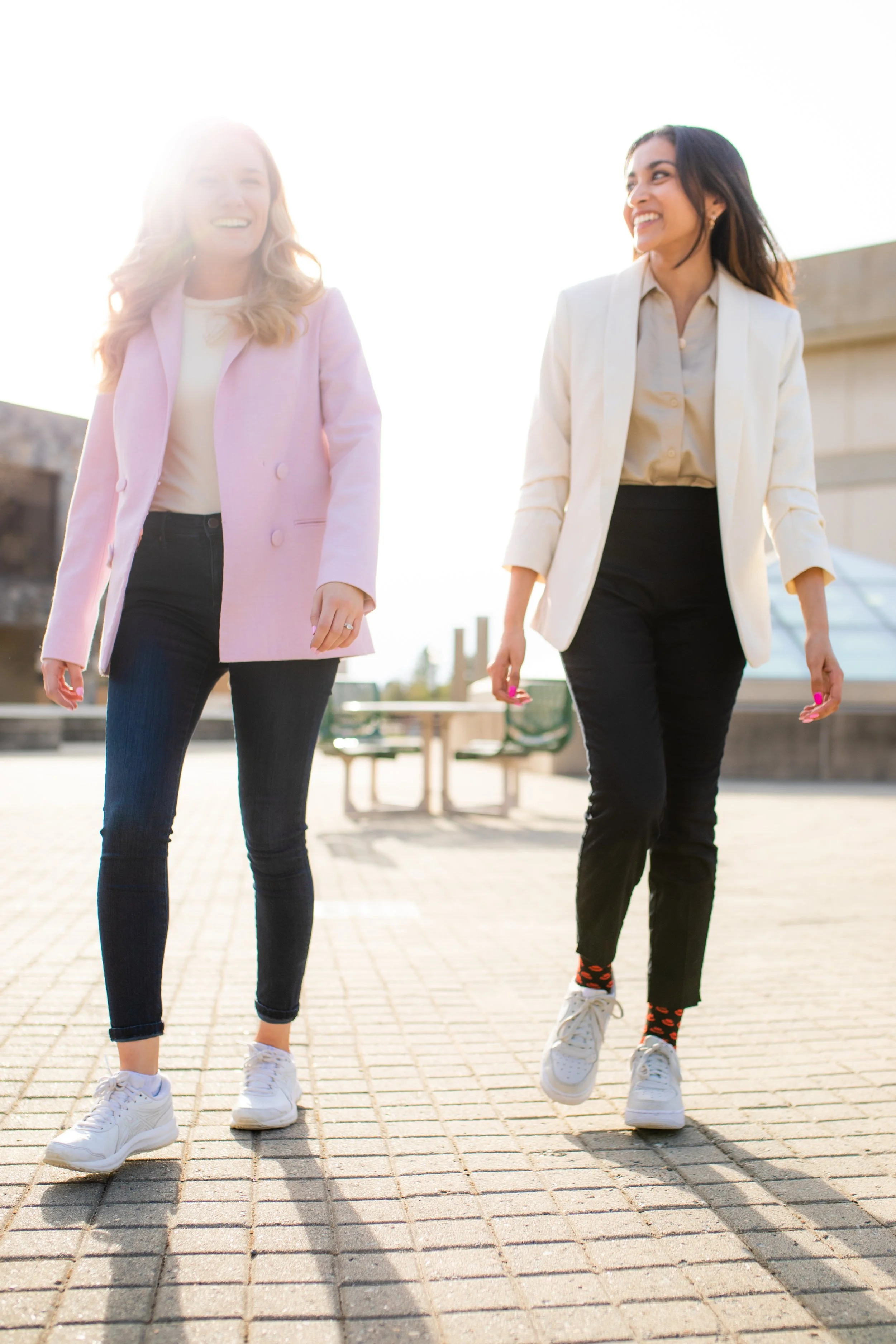Two women walking outdoors on a sunny day, smiling and talking.