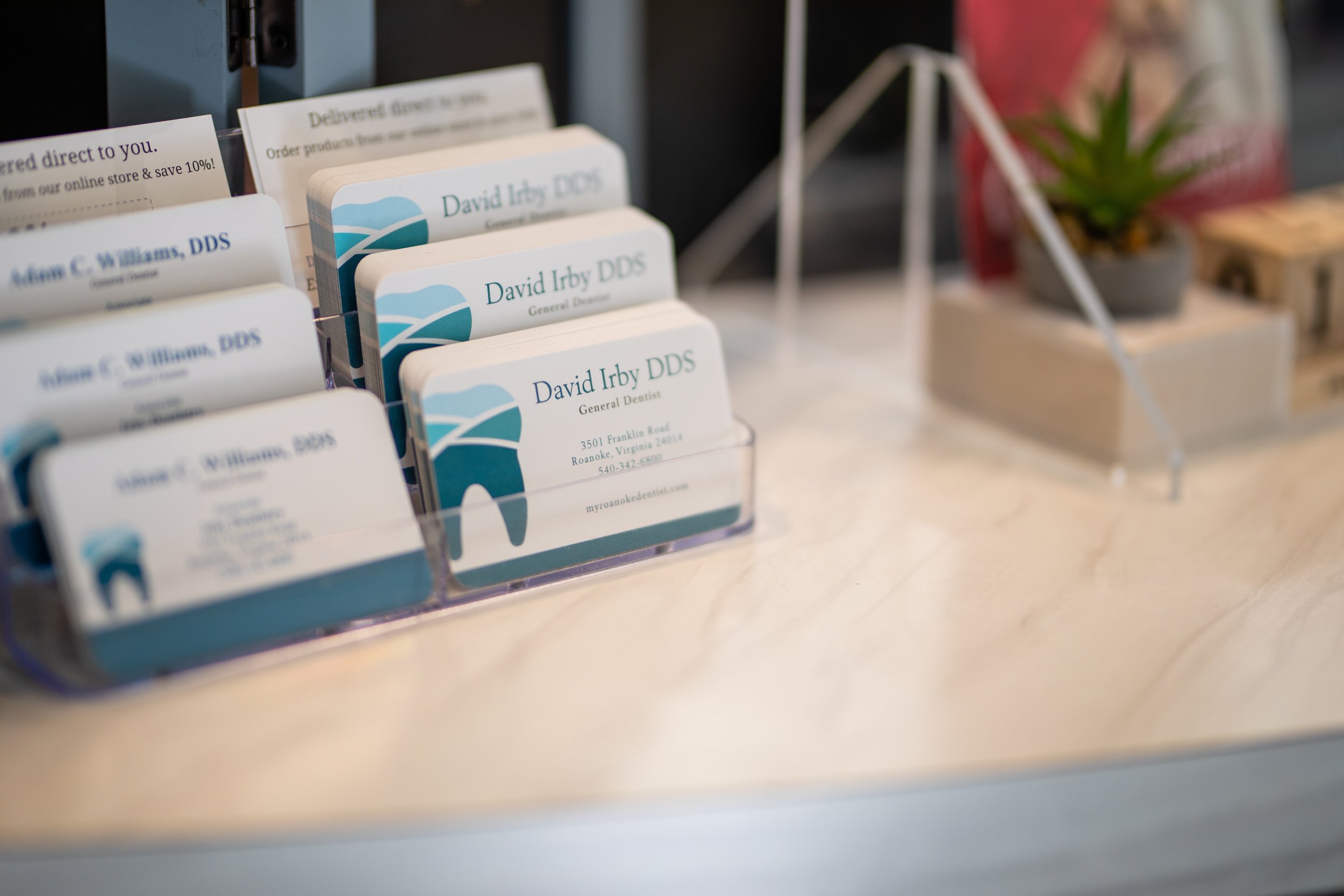 Business cards for David Irby DDS, a general dentist, in a holder on a marble countertop, with a small potted plant and other items in the background.