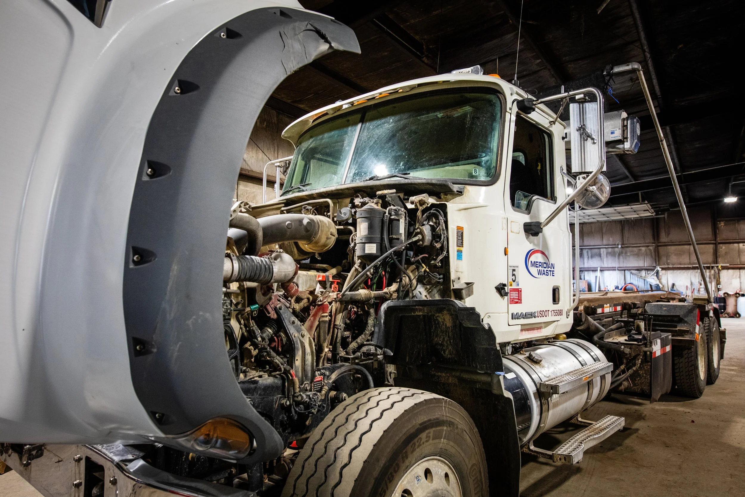A semi-truck with its front engine components exposed inside a warehouse.