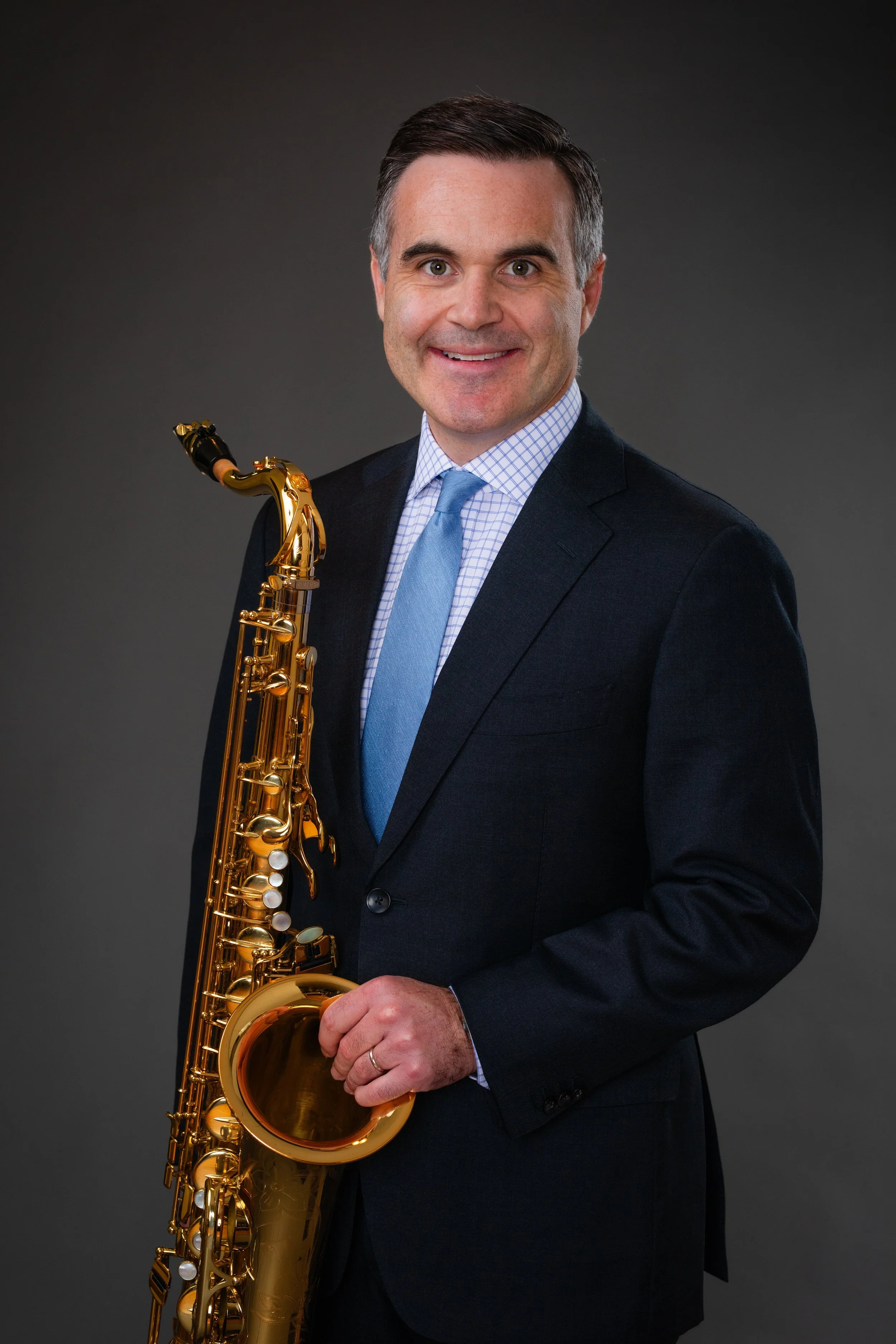 Man in a suit holding a golden saxophone smiling at the camera.