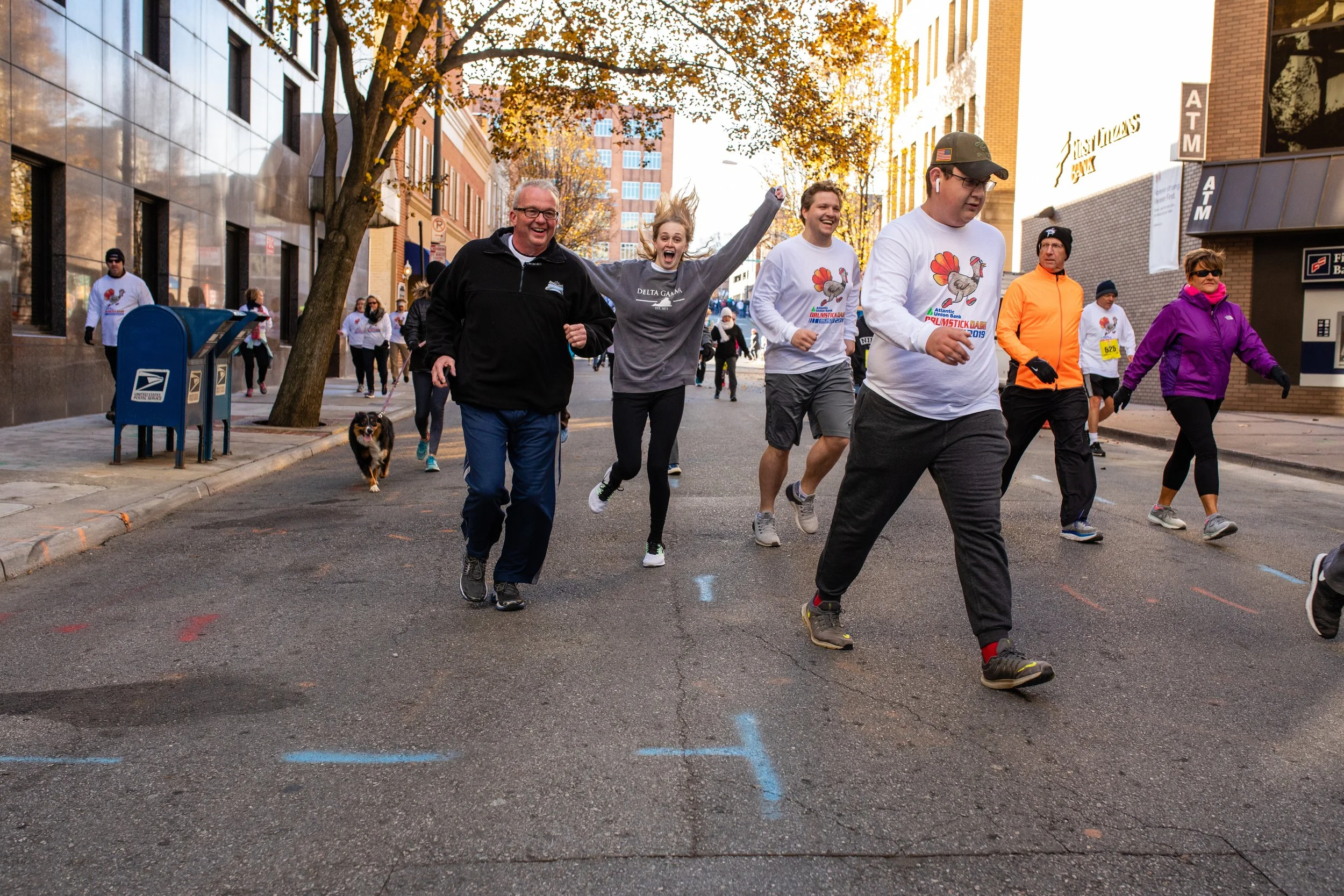 People running in a city street during a race or marathon, smiling and appearing joyful on a sunny day.
