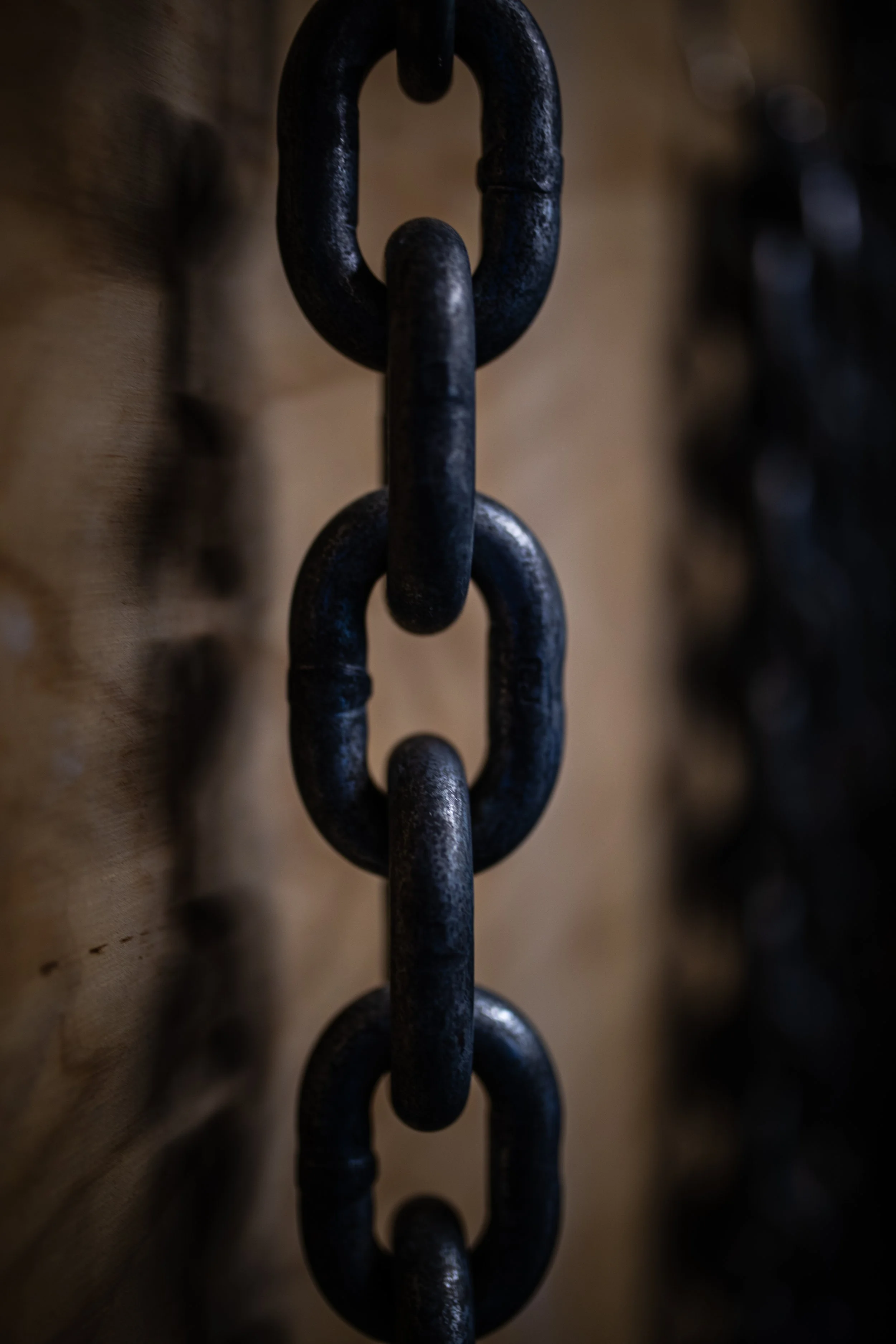Close-up of a black metal chain hanging vertically, with a wooden background.