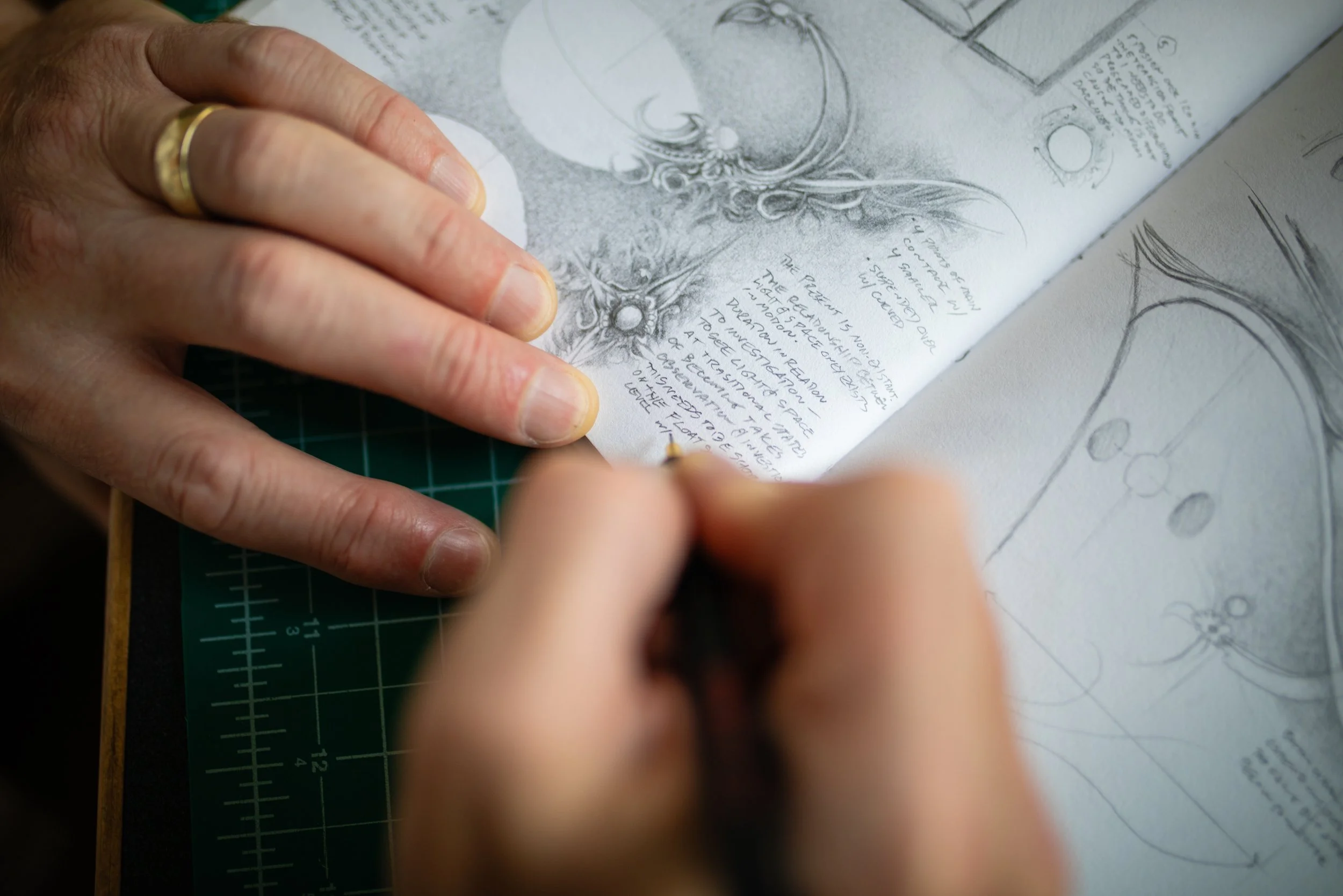 A person is sketching and writing in a notebook, which contains anatomical drawings and handwritten notes, on a green cutting mat.