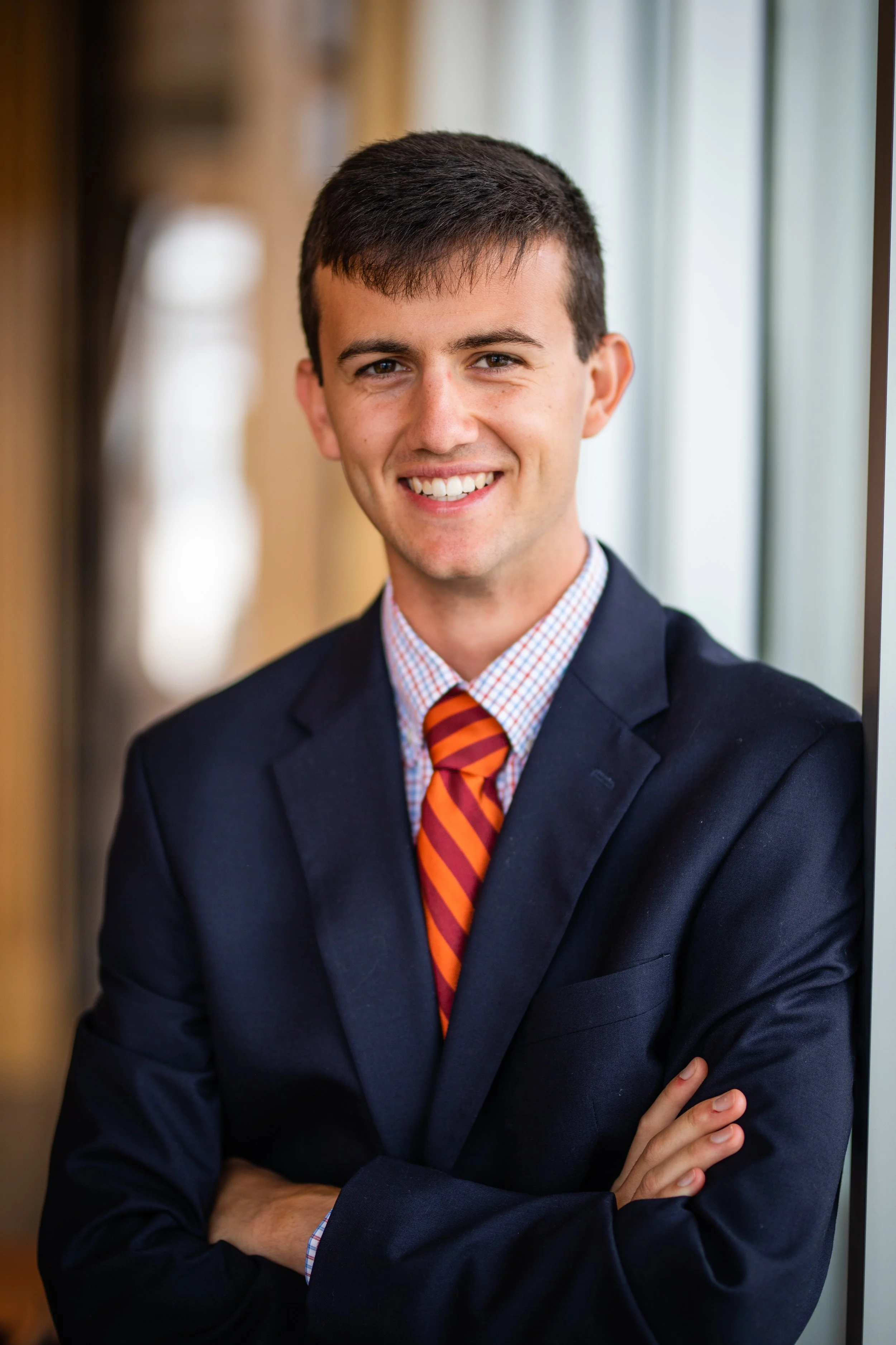 Portrait of a young man in a suit with crossed arms, smiling, in a professional setting.
