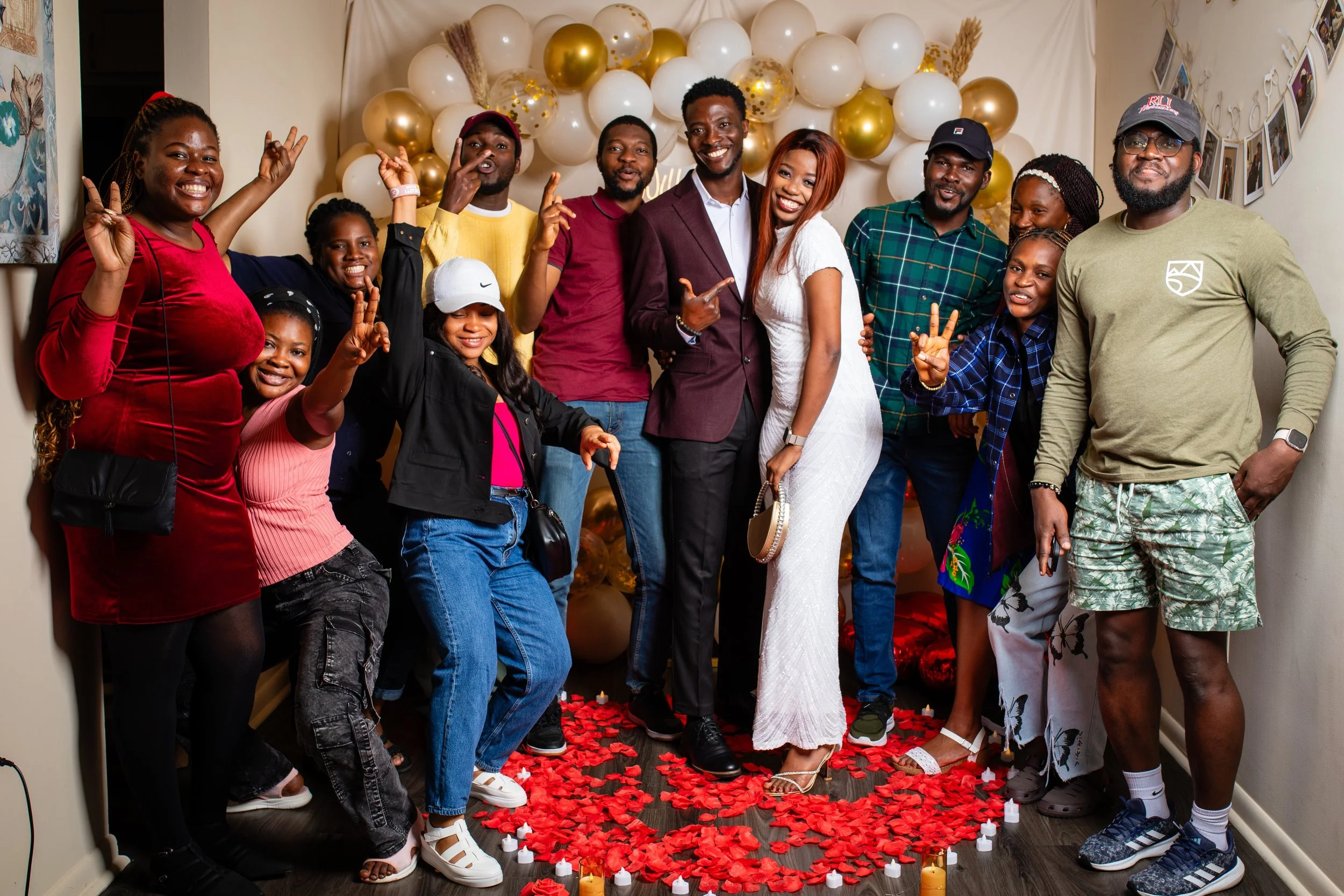 Group of people celebrating together at a party with balloons and rose petals on the floor.