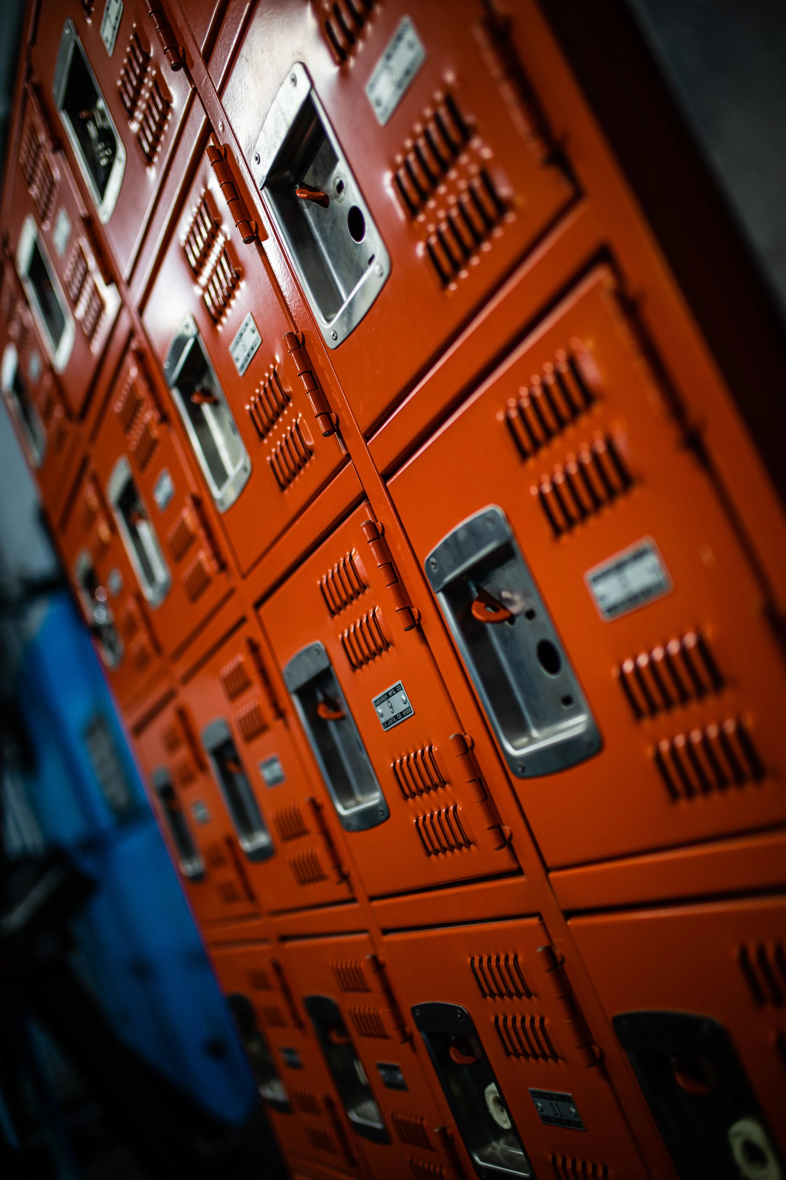 Several orange lockers with vents and metal handles, arranged in a row on a wall.