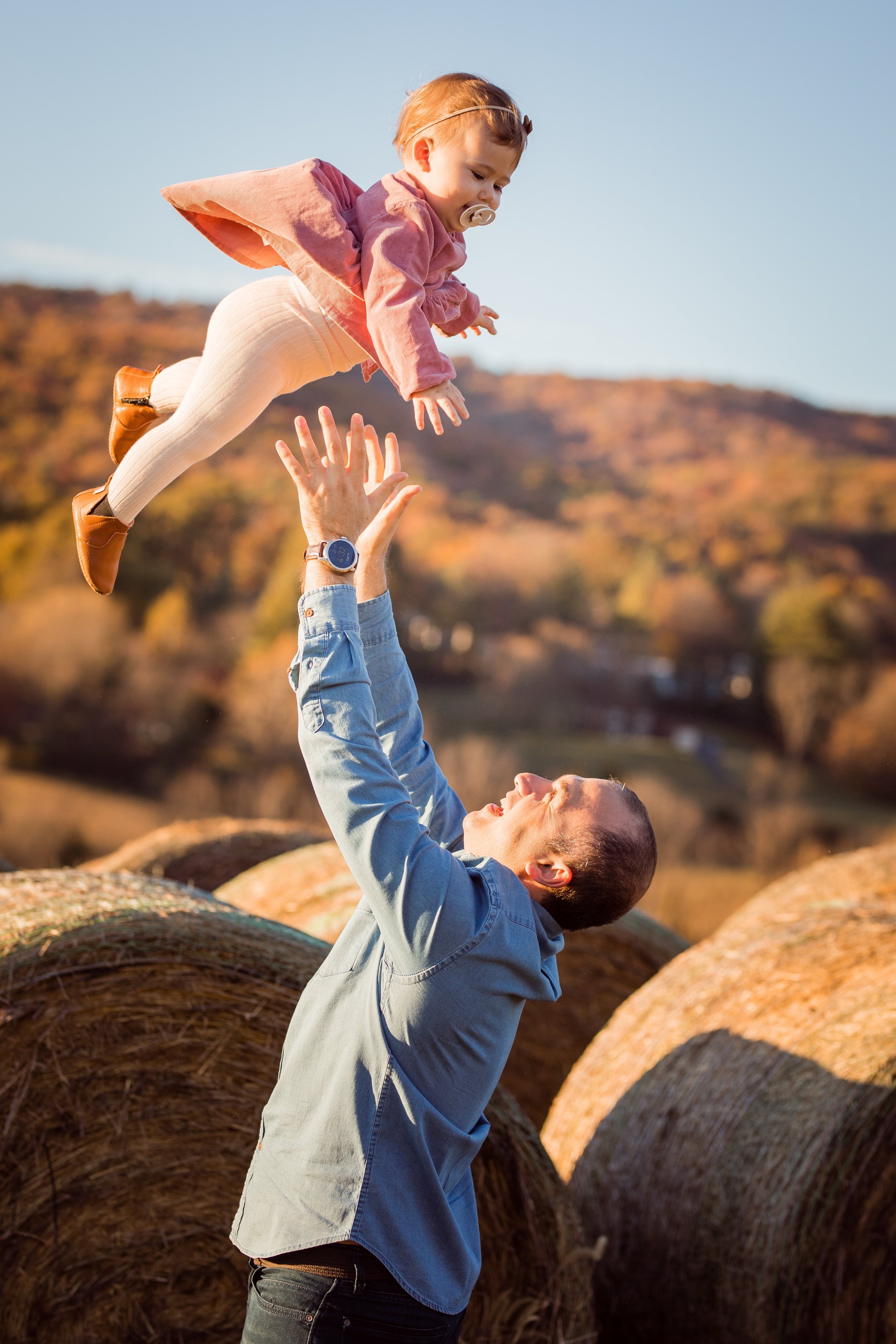 A man lifting a young girl in the air outdoors during autumn.