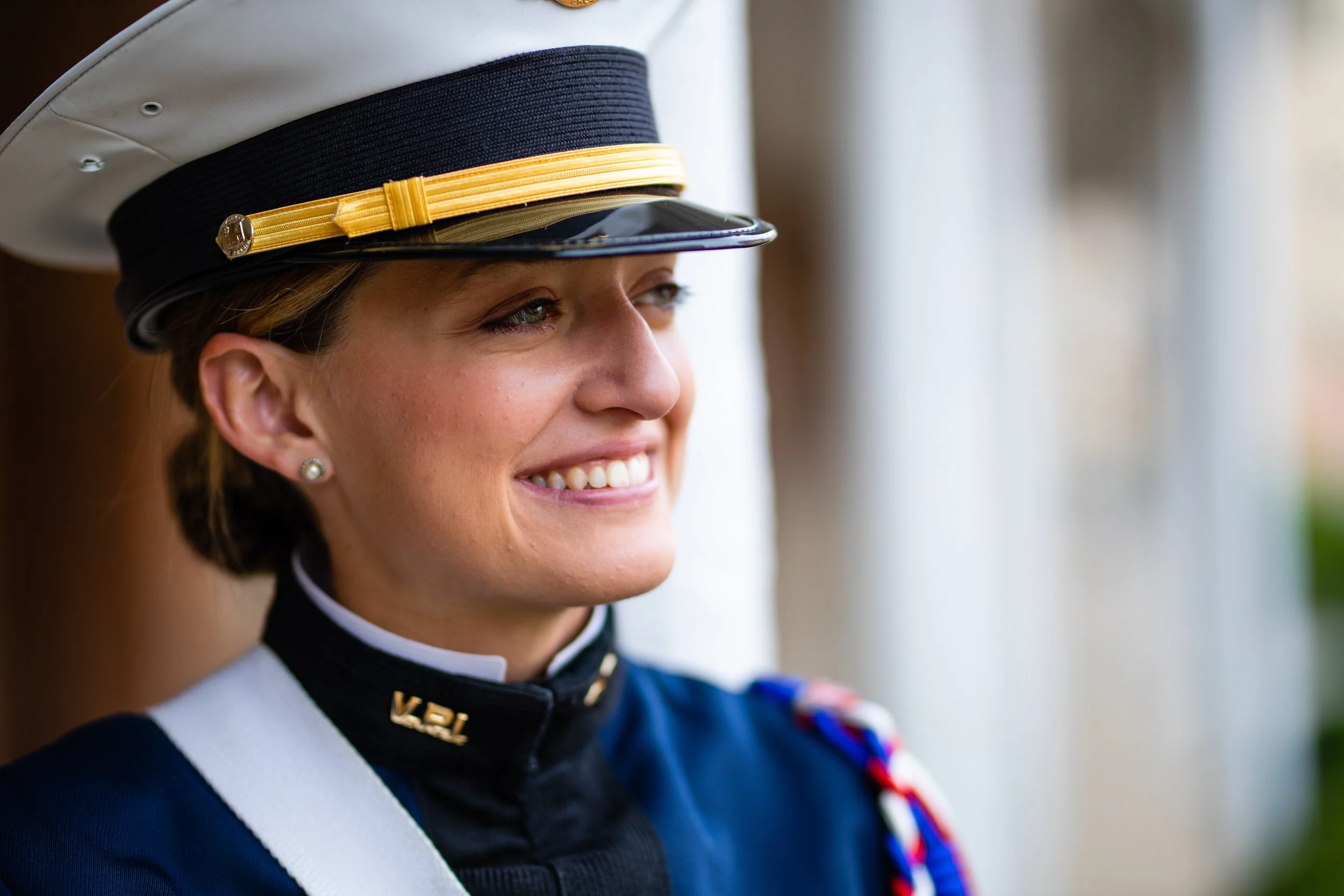 Close-up of a female military officer smiling, wearing a formal uniform and a peaked cap with a gold and black band.