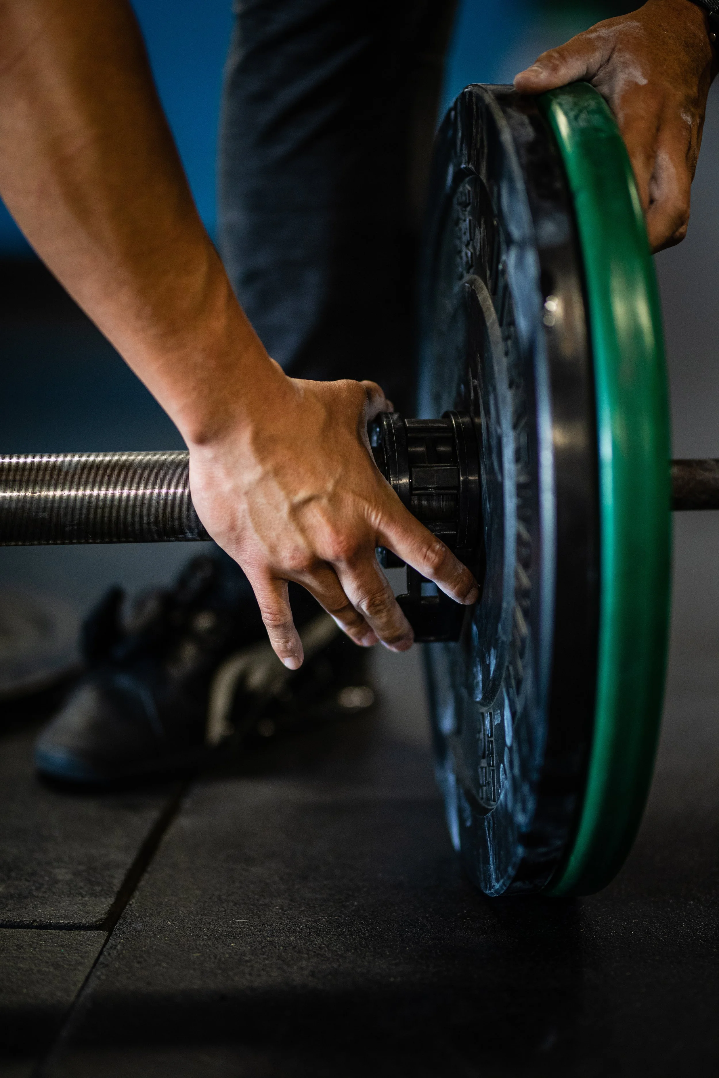 Person setting up a weight plate on a barbell in a gym.