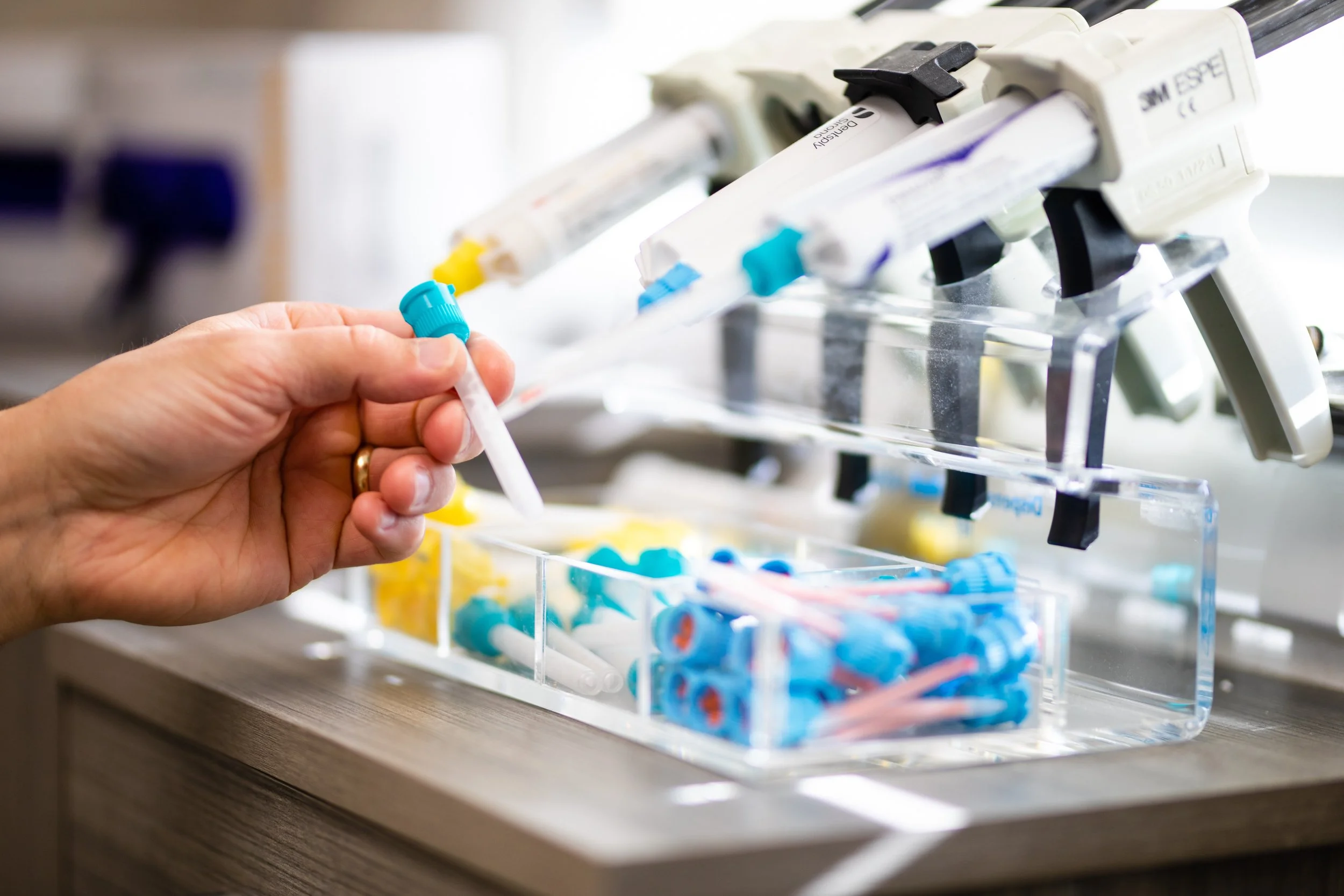 Close-up of a hand holding a syringe near a box of medical syringes and liquids in a clinical setting.