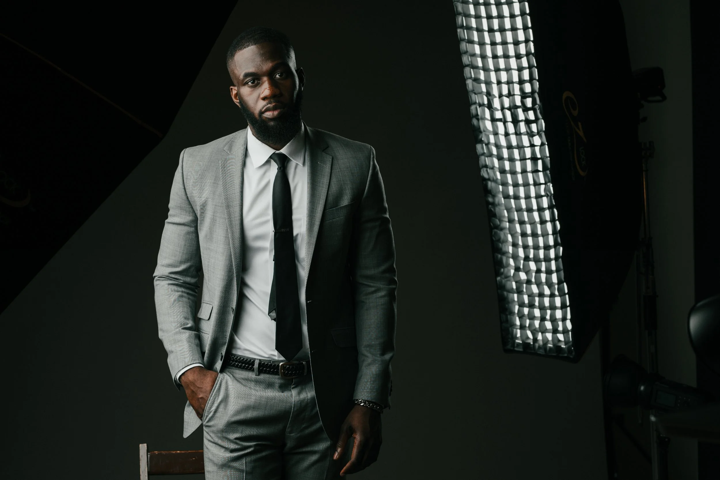 A man in a gray suit and black tie standing in a photography studio with lighting equipment.