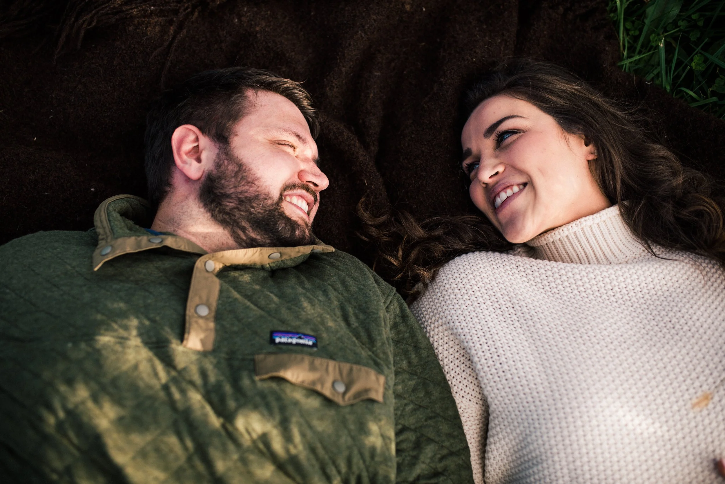 A man and woman lying on the ground, looking at each other and smiling.